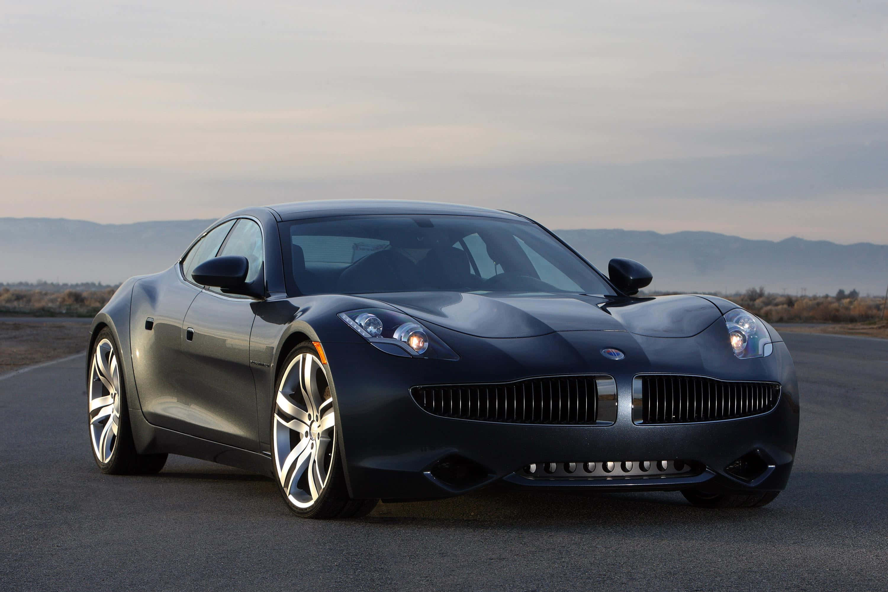 Fisker Karma 豪華電動車，沿海風光之旅 壁紙 — 一架時尚的啞光黑色跑車配銀色輪圈，停在黎明時分空無一人的道路上，背景是朦朧的山巒。