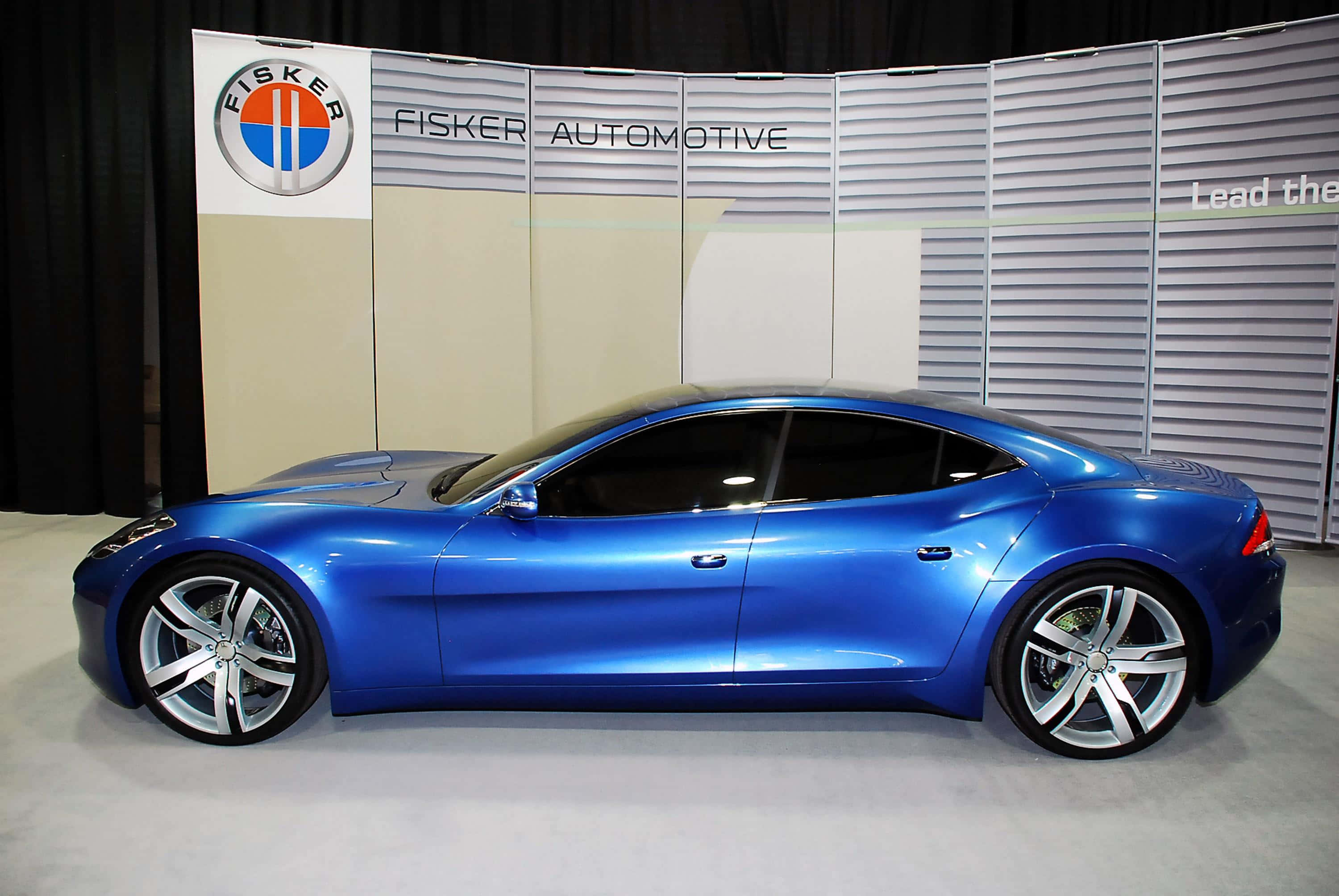 Fisker Karma 電動車在開闊道路上行駛 壁紙 — 一輛時尚的藍色Fisker概念車在室內車展的明亮燈光下閃耀。
