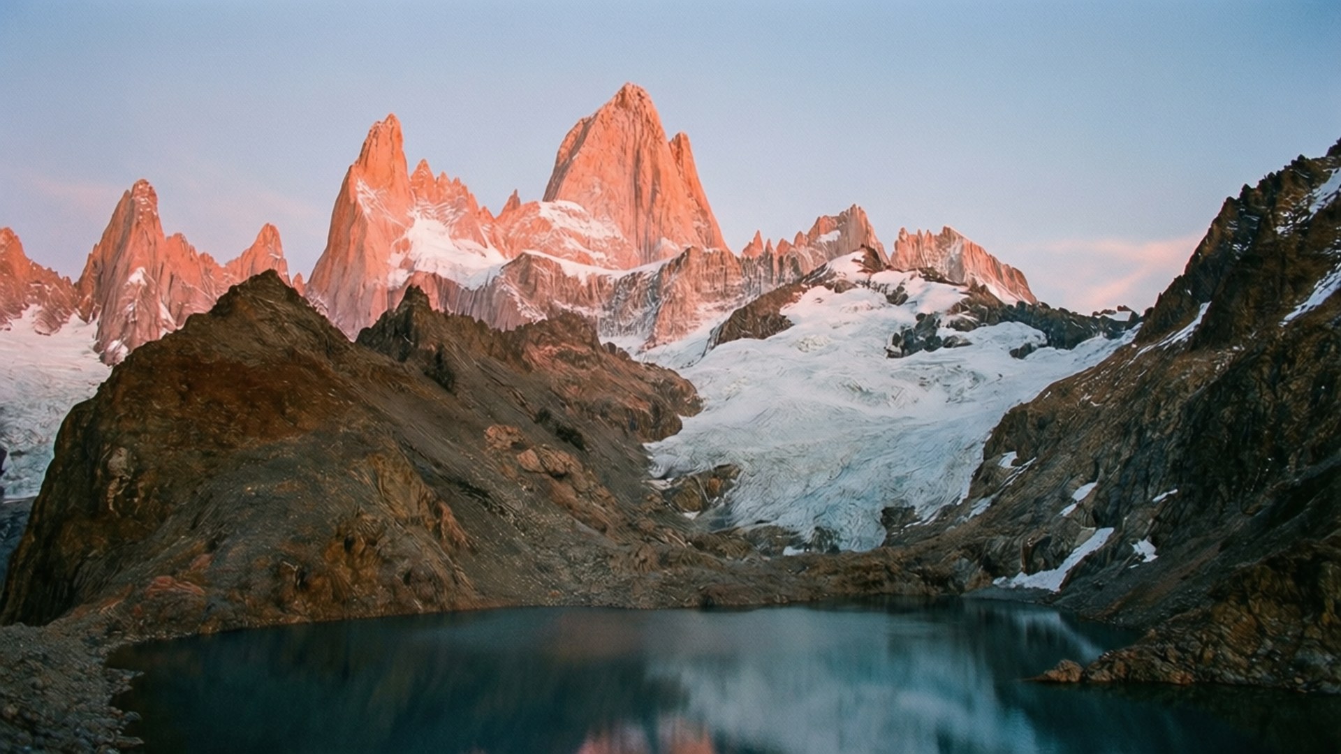 鋸齒狀的雪山在日落時分倒映在平靜的高山湖泊中。