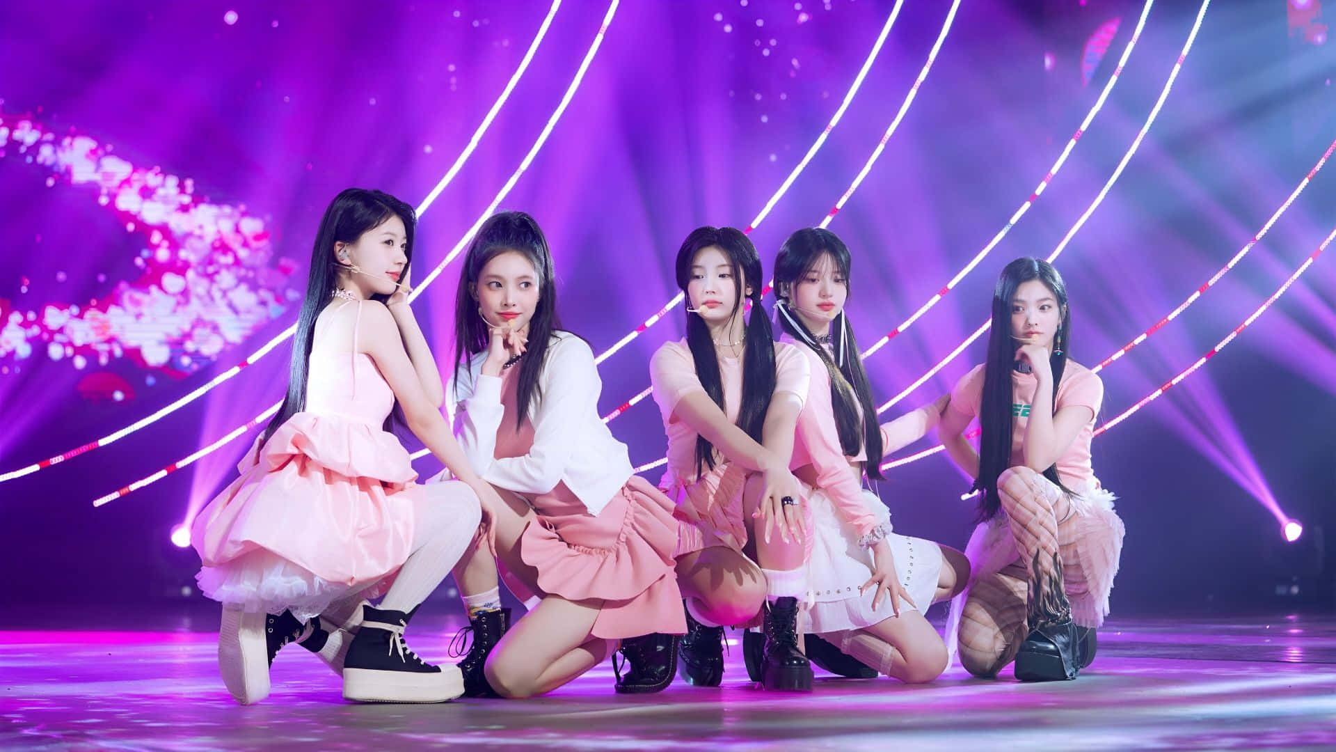  壁紙 — 五位身穿粉紅色服裝的女表演者在發光的紫色舞台上動態擺姿勢，舞台上有彎曲的光束和閃爍效果。