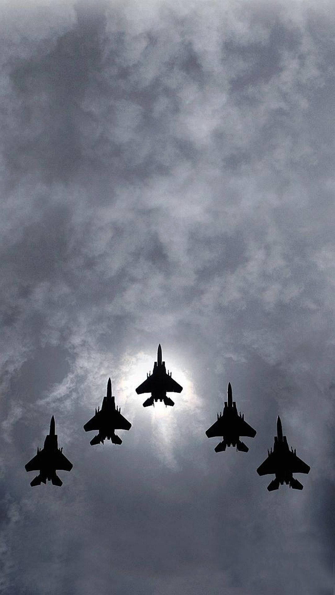 五架戰鬥機在多雲天空中以編隊飛行，太陽在它們背後。