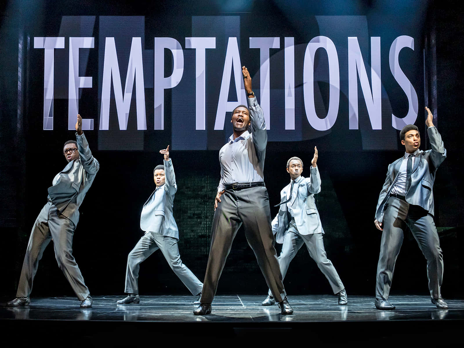  壁紙 — 五位身穿銀色西裝的男表演者在一個大型「TEMPTATIONS」標誌下的舞台上擺出同步姿勢。