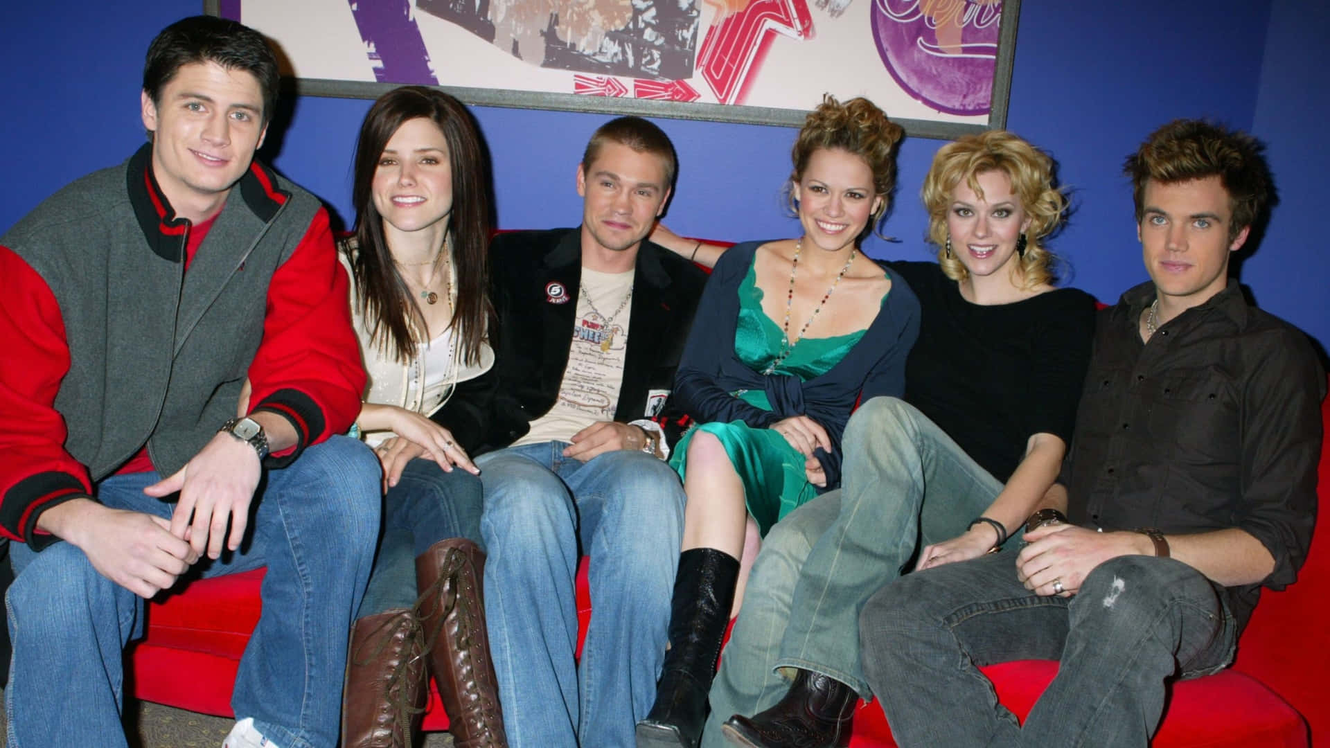  壁紙 — 來自《The O.C.》的五位年輕演員坐在紅色梳化上，背後是藍色牆壁和裱框藝術品，對著鏡頭微笑。