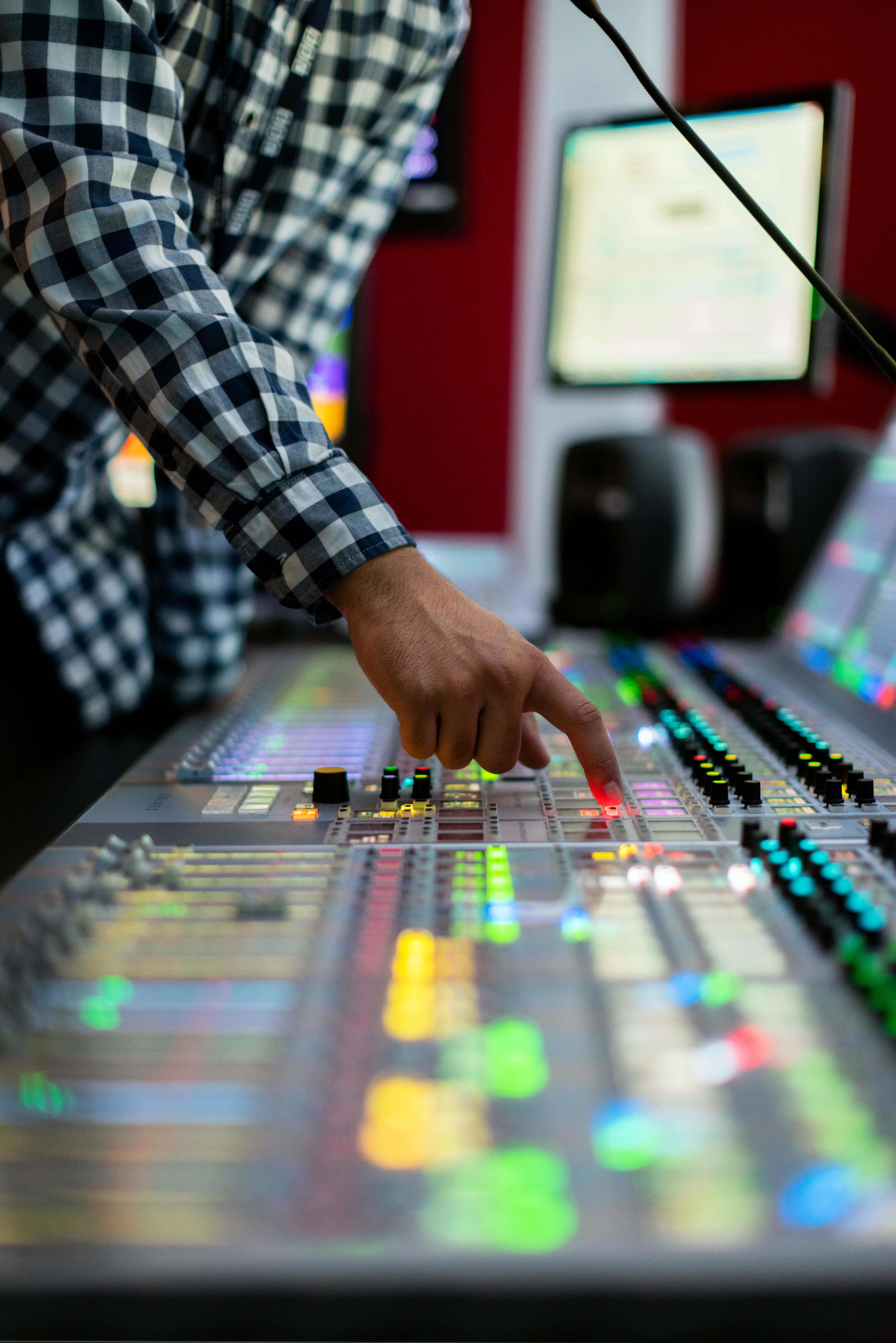 FL Studio 音效控制器 壁紙 — 一位穿著格仔衫的人正在調整錄音室專業音頻混音控制台上發光的推子。