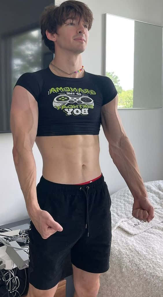 一位身材健美的年輕男子在臥室裡穿著遊戲主題的短版上衣擺姿勢。