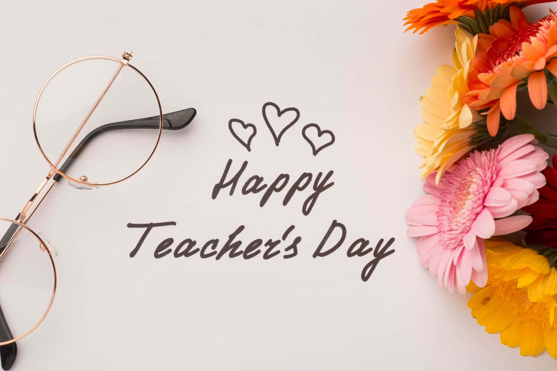  壁紙 — 玫瑰金眼鏡、手寫Happy Teacher's Day文字配心心、白色背景上鮮豔的非洲菊雛菊花束的平鋪擺放。