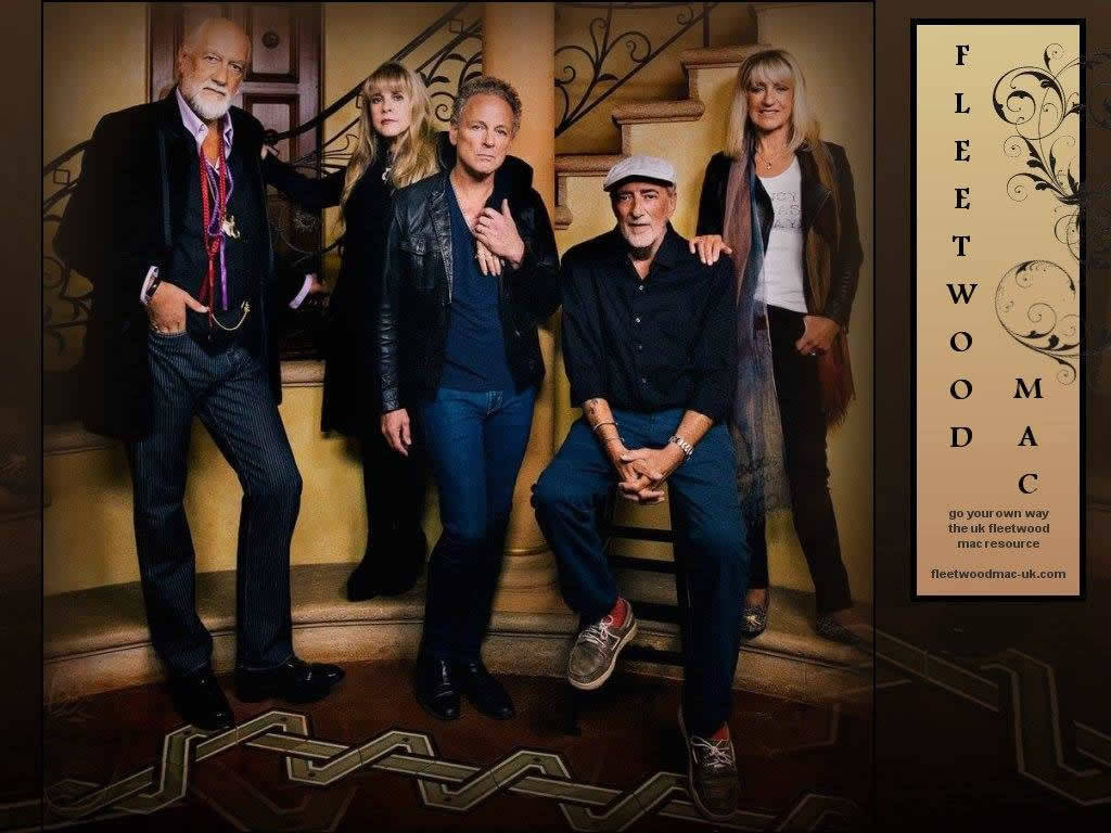 Fleetwood Mac 五人原班陣容 壁紙 — Fleetwood Mac 樂隊成員在溫暖燈光的復古室內環境中，自信地站在裝飾華麗的樓梯上，樓梯有裝飾欄杆和圖案地板。