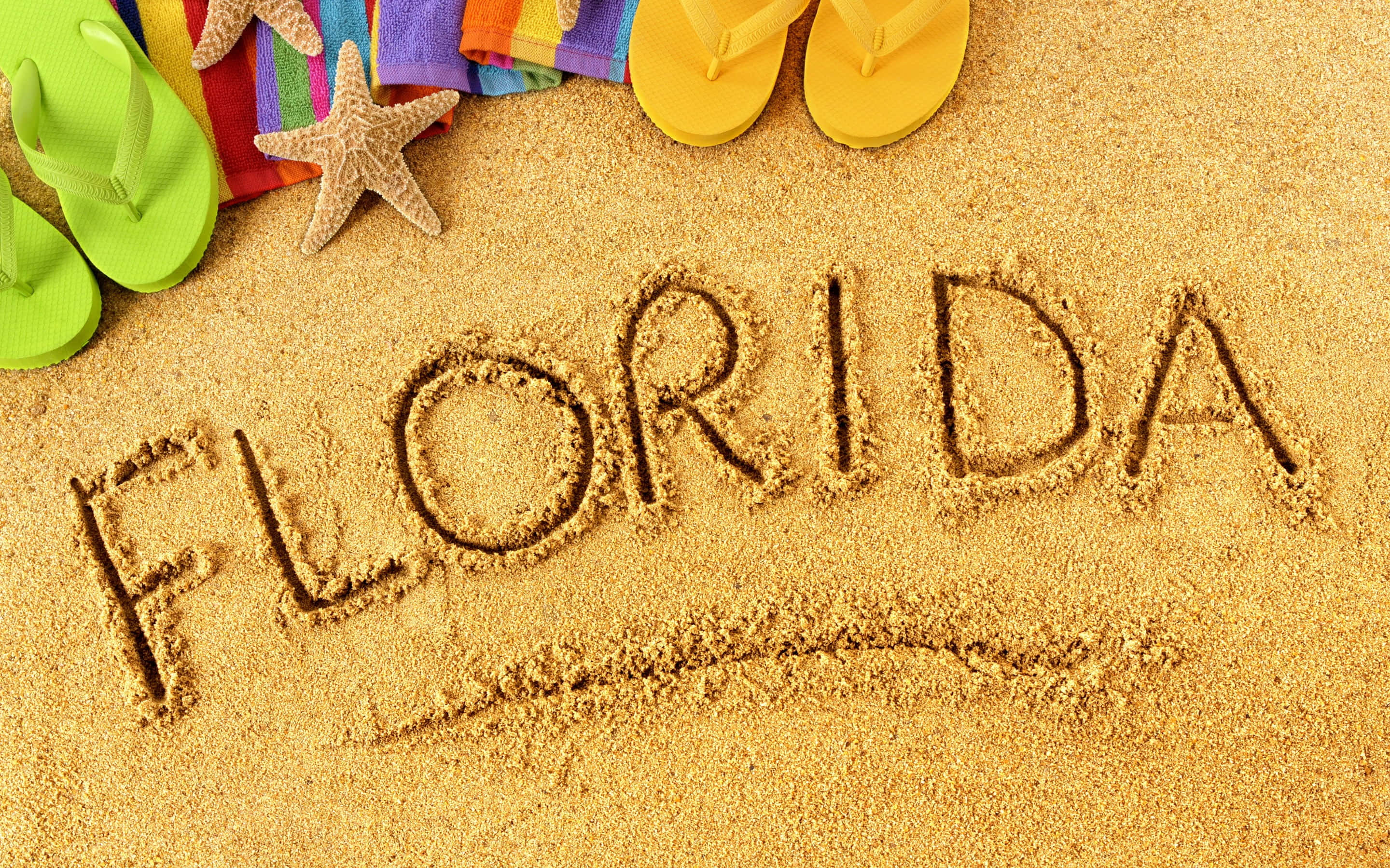 Beach Accessories 桌布 壁紙 — 「FLORIDA」呢個字用金色沙寫喺彩色人字拖、海星同彩虹毛巾旁邊。