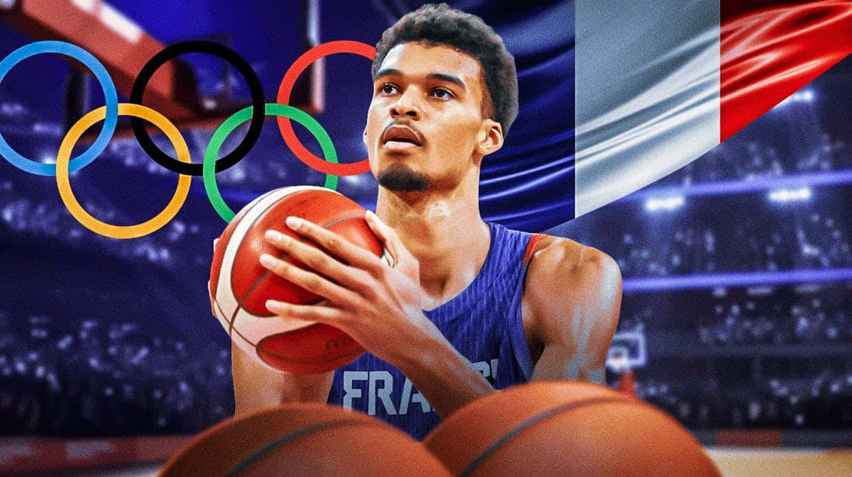  壁紙 — 一位專注的法國籃球運動員在體育館的奧運五環和旗幟下持球。
