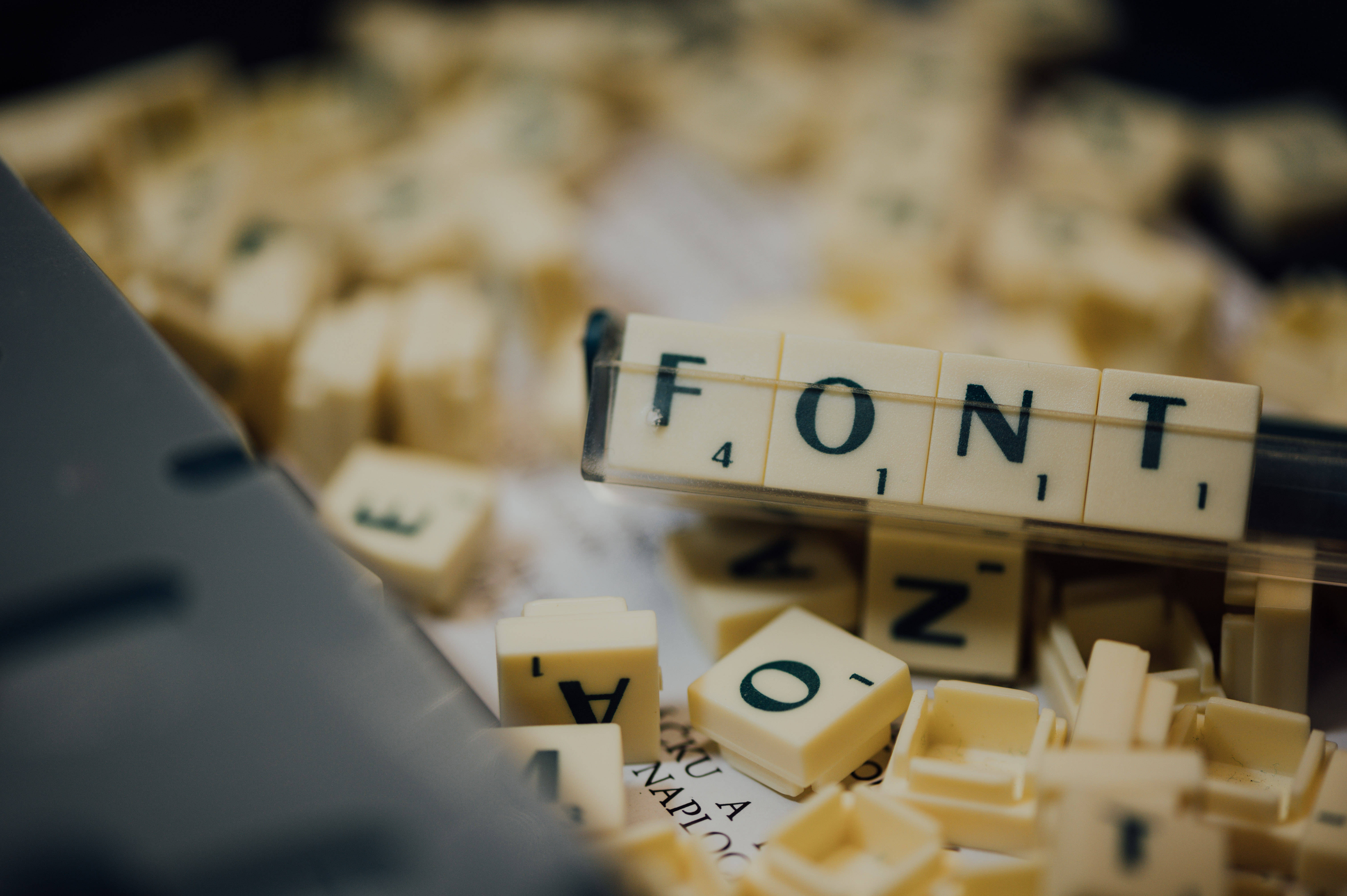 標題：拼字遊戲方塊拼出「FONT」字樣 壁紙 — 奶油色 Scrabble 字母塊的特寫，拼出 FONT，背景有模糊的鍵盤。