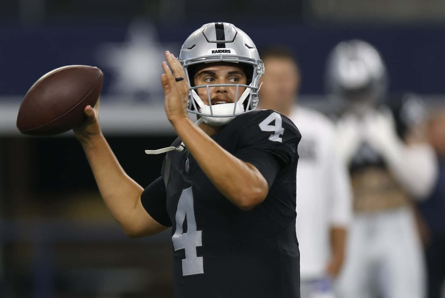  壁紙 — 一名身穿黑色Raiders球衣、背號4的美式足球四分衛在球場燈光下準備在比賽中傳球。