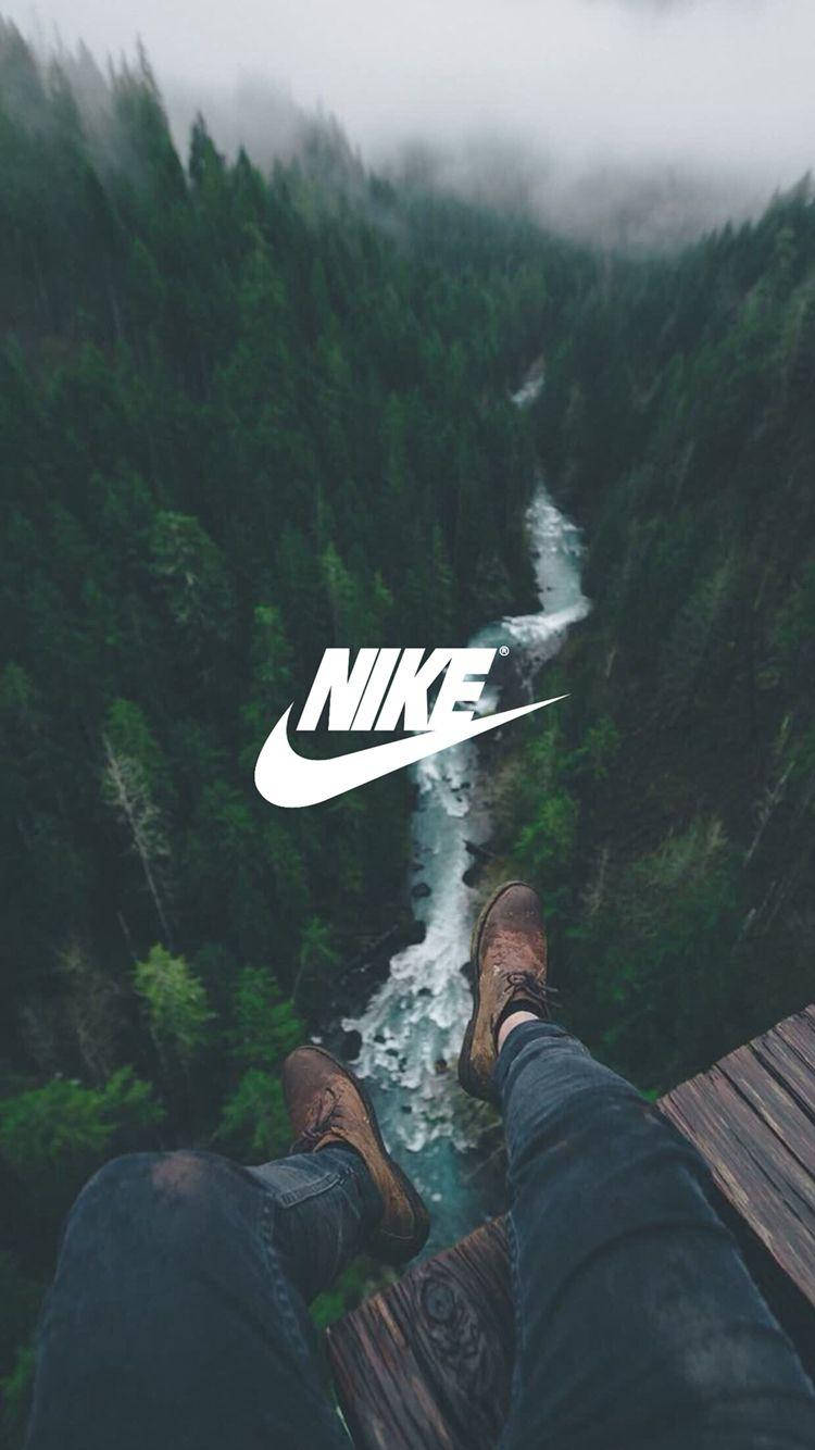 Forests Nike iPhone Logo 壁紙 — 一個人的腳穿著靴子懸掛在木製平台上，俯瞰著霧氣瀰漫的森林峽谷，下方有湍急的河流。