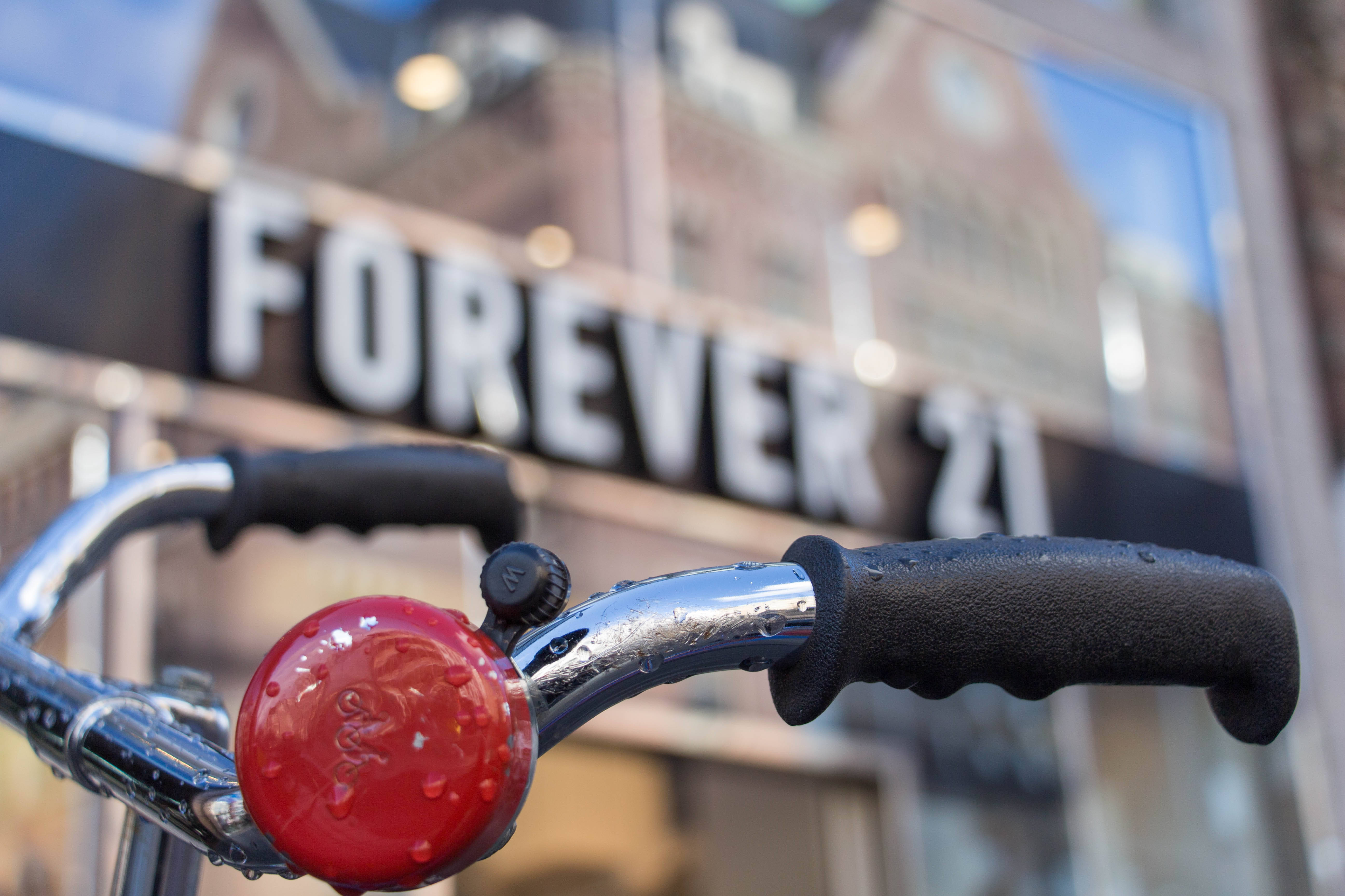 Forever 21 商店 壁紙 — 模糊嘅Forever 21商店櫥窗前，一個濕嘅單車把手連紅色鈴鐺同黑色手柄嘅特寫。