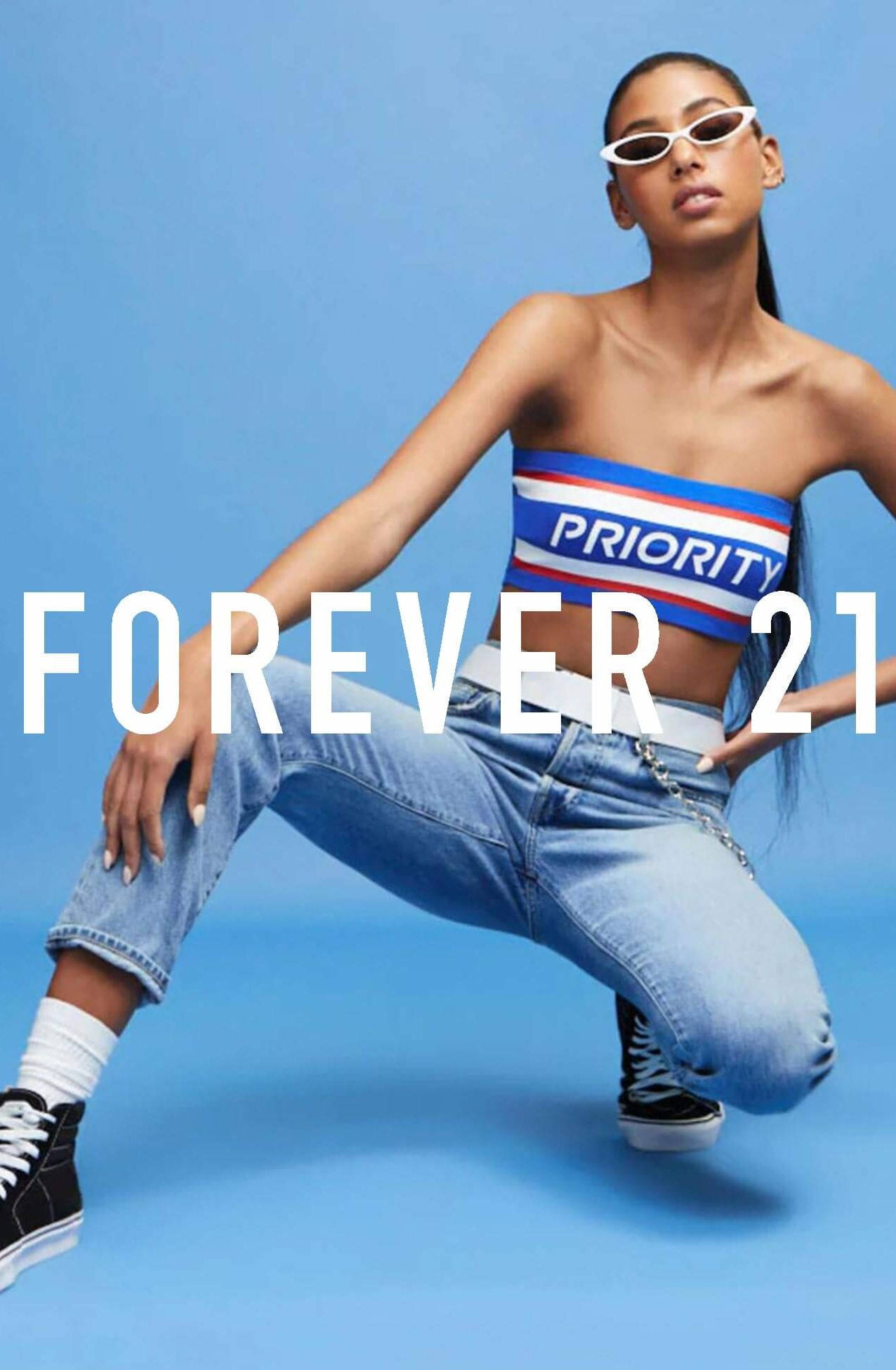 Forever 21 時尚服飾海報 壁紙 — 一位時尚女性身穿條紋露臍上衣和牛仔褲，在純藍色攝影棚背景前自信地擺姿勢。