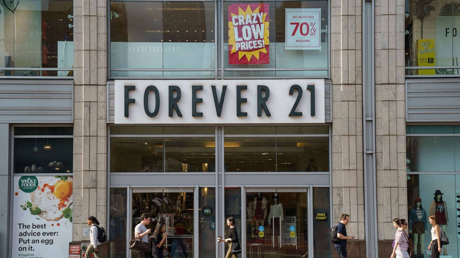 Forever 21 時尚零售精品店 壁紙 — 一條繁忙的城市街道上有一間Forever 21商店，帶有醒目的招牌，購物者經過展示人體模型和促銷海報的玻璃櫥窗。