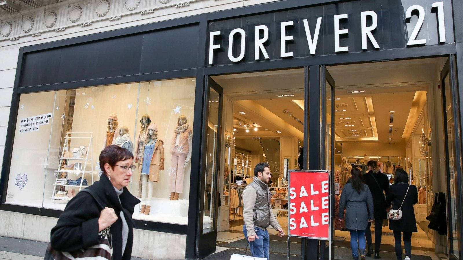 Forever 21 美國零售店 壁紙 — 購物者進出一間Forever 21商店，店內有明亮的減價標誌和櫥窗展示的人體模型。