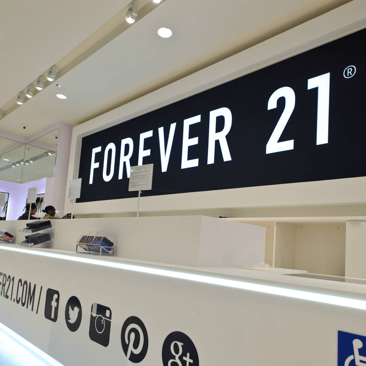 Forever 21收銀台 壁紙 — 明亮現代的Forever 21店內，白色櫃檯上有一個大型黑色招牌，上面有白色粗體字和社交媒體圖標。