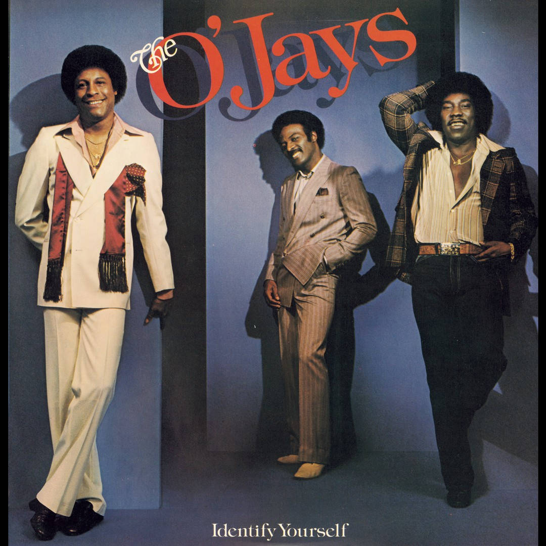Forever Mine 音樂 Ojays 壁紙 — 三位微笑的男士穿著時尚的1970年代西裝，在藍色工作室背景前自信地擺姿勢，帶有'The O'Jays'標誌。