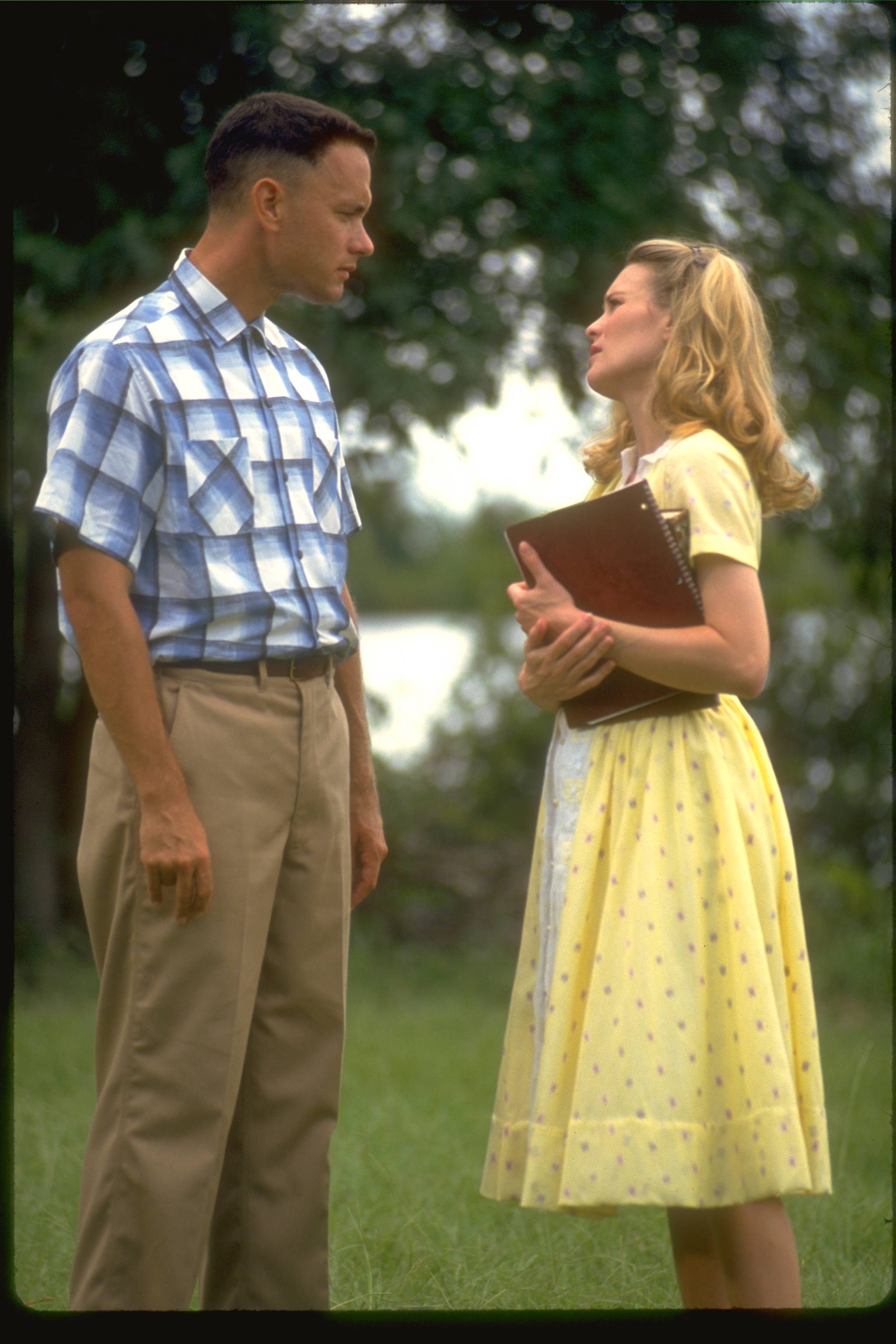 Forrest Gump 面對 Jenny 壁紙 — 一名穿著藍色格仔恤衫的男子和一名穿著黃色圓點裙的女子在樹下的草地上相對而立。