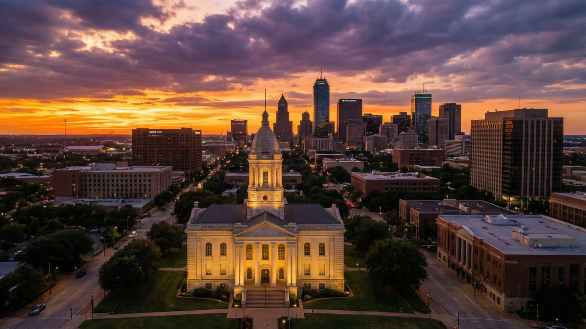 Fort Worth Sunset Skyline 壁紙 — 一座宏偉的新古典主義法院在日落時分溫暖地發光，襯托著現代城市天際線上方充滿活力的紫色和橙色天空。