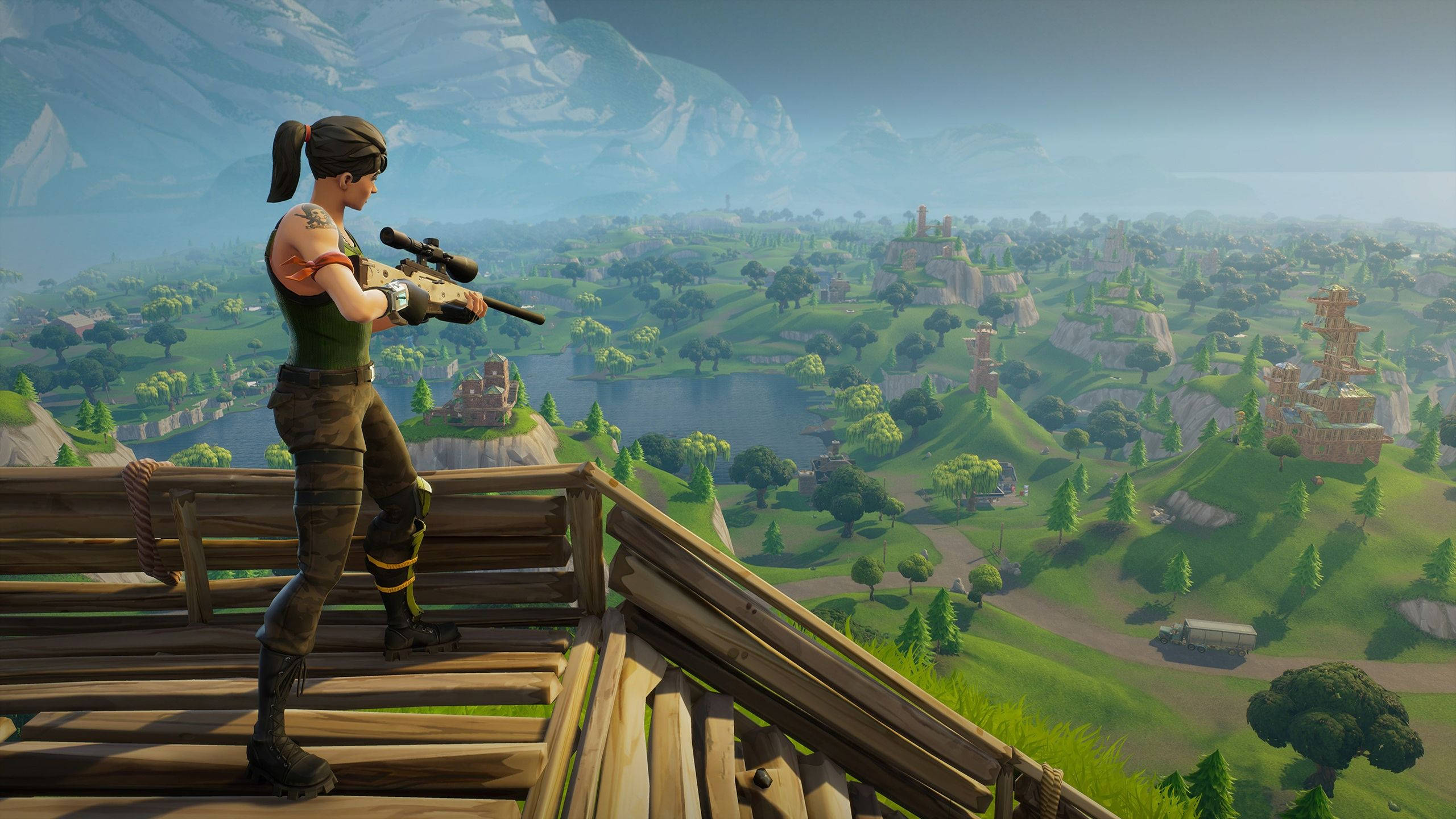 Fortnite 2560x1440 木製哨站狙擊 壁紙 — 一個Fortnite角色站在木製瞭望台上，用狙擊步槍瞄準一片廣闊的綠色景觀，其中有湖泊、城堡和遠山。