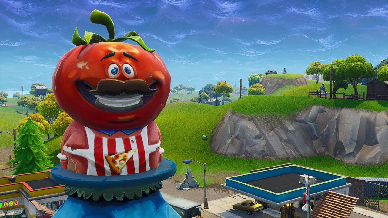 Fortnite 火力全開 番茄鎮 壁紙 — 一個戴著鬍鬚和披薩片圍裙的巨型卡通番茄，站在色彩繽紛的Fortnite風格景觀中，有起伏的山丘和岩石懸崖。