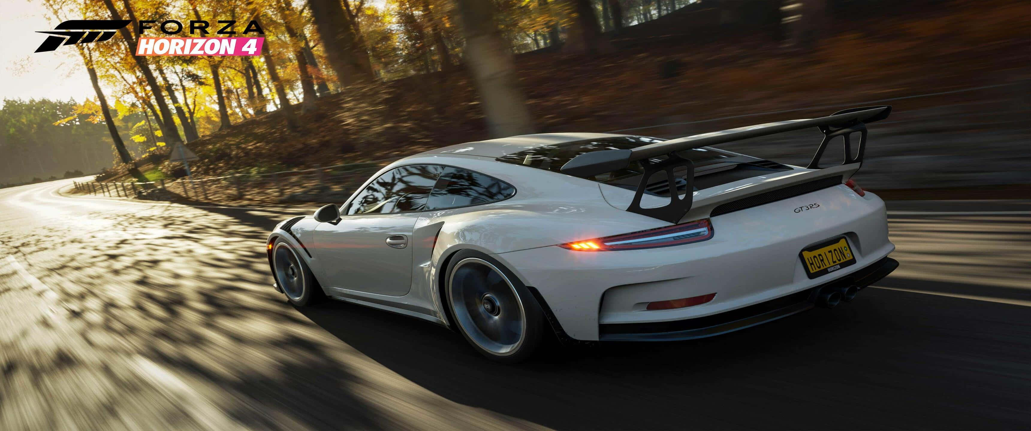 《Forza Horizon 4》遊戲 3440x1440p 超寬背景 壁紙 — 一輛白色保時捷911 GT3 RS在陽光明媚的秋日森林中疾馳，道路上呈現動態模糊效果。
