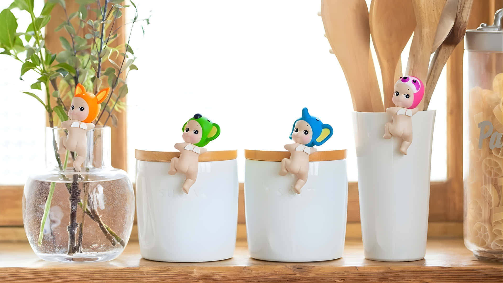  壁紙 — 四個戴動物帽的可愛公仔緊貼在木製枱面上的廚房容器上，旁邊有一盆植物和一個意粉罐。