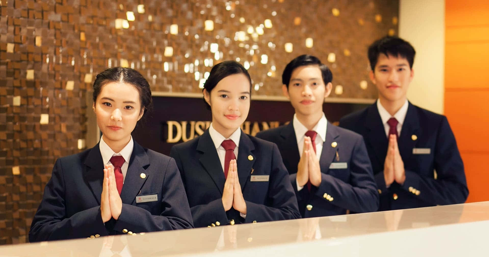 四名身穿正式制服的酒店員工雙手合十歡迎客人。