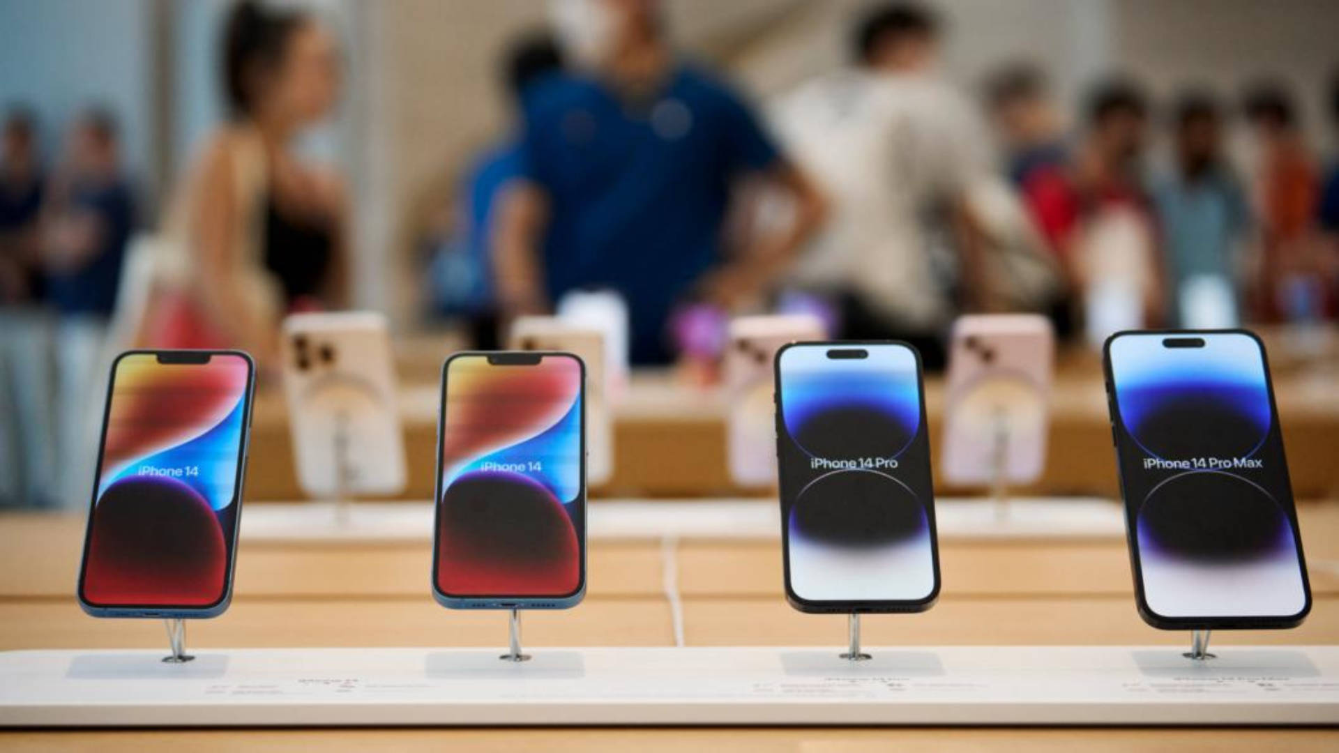 店內展示架上的四部 iPhone 14 型號，背景有人群。