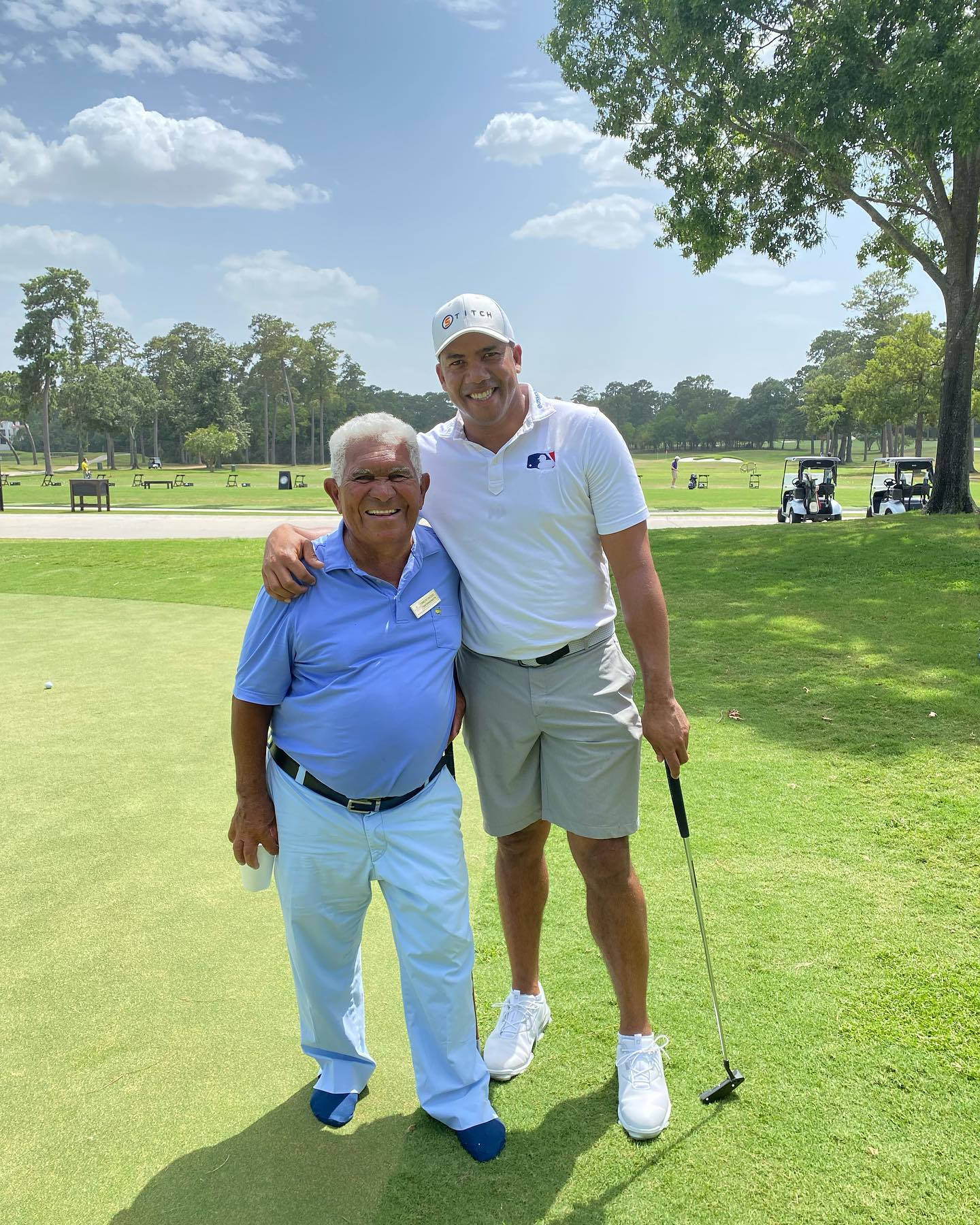 Franci Betancourt 與 Jhonattan Vegas 壁紙 — 兩位微笑嘅男士喺陽光普照嘅高爾夫球場上擺姿勢，周圍有茂密嘅綠草同樹木，背景係明亮嘅藍天。