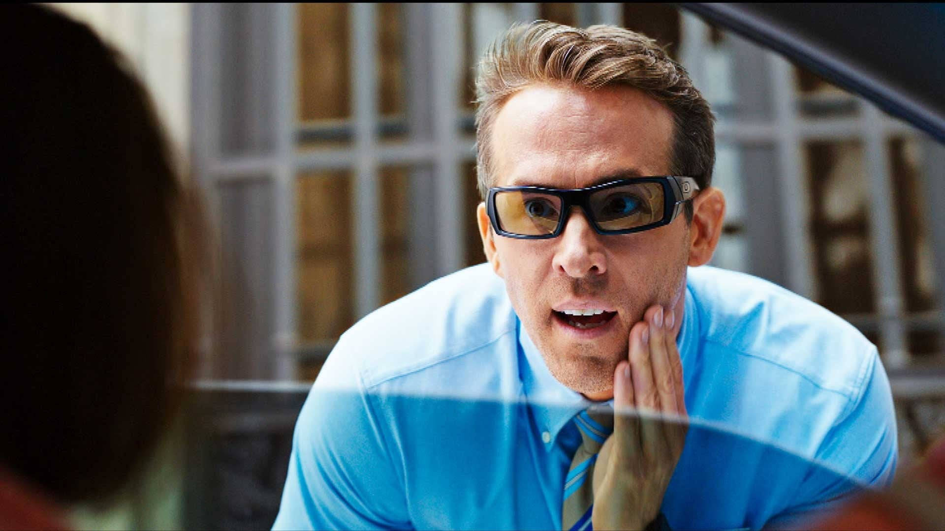 瑞安·雷諾茲《Free Guy》佩戴 Oakley 太陽眼鏡 壁紙 — 一名身穿藍色襯衫、戴著3D眼鏡的男子，手托臉頰，身體前傾，表情震驚。