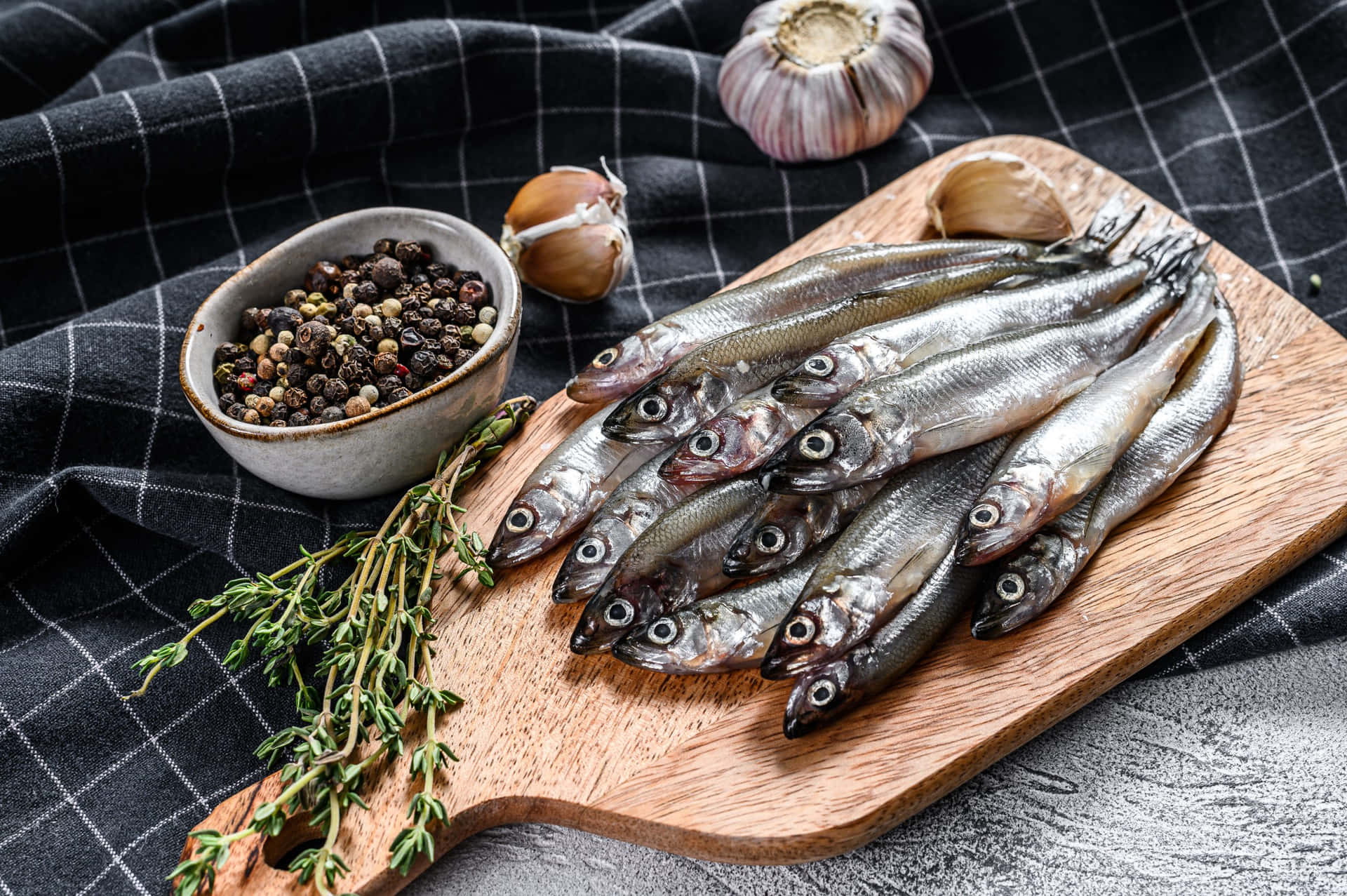  壁紙 — 新鮮小魚排列在木砧板上，配上大蒜、百里香和胡椒粒，置於格仔布上。