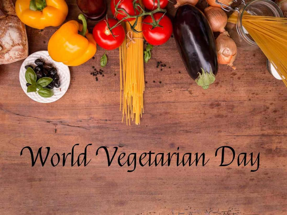  壁紙 — 新鮮蔬菜和意粉擺放在質樸的木桌上，帶有'World Vegetarian Day'文字。