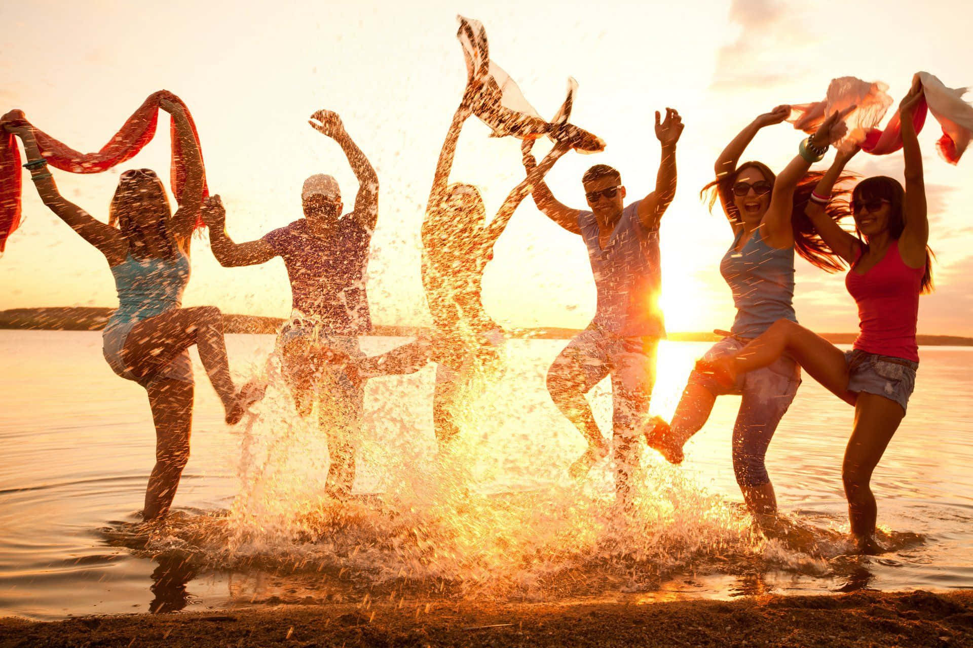 Beach Dance Party 桌布 壁紙 — 朋友們在金色夕陽的水中歡樂跳躍，在他們周圍激起閃閃發光的水花。