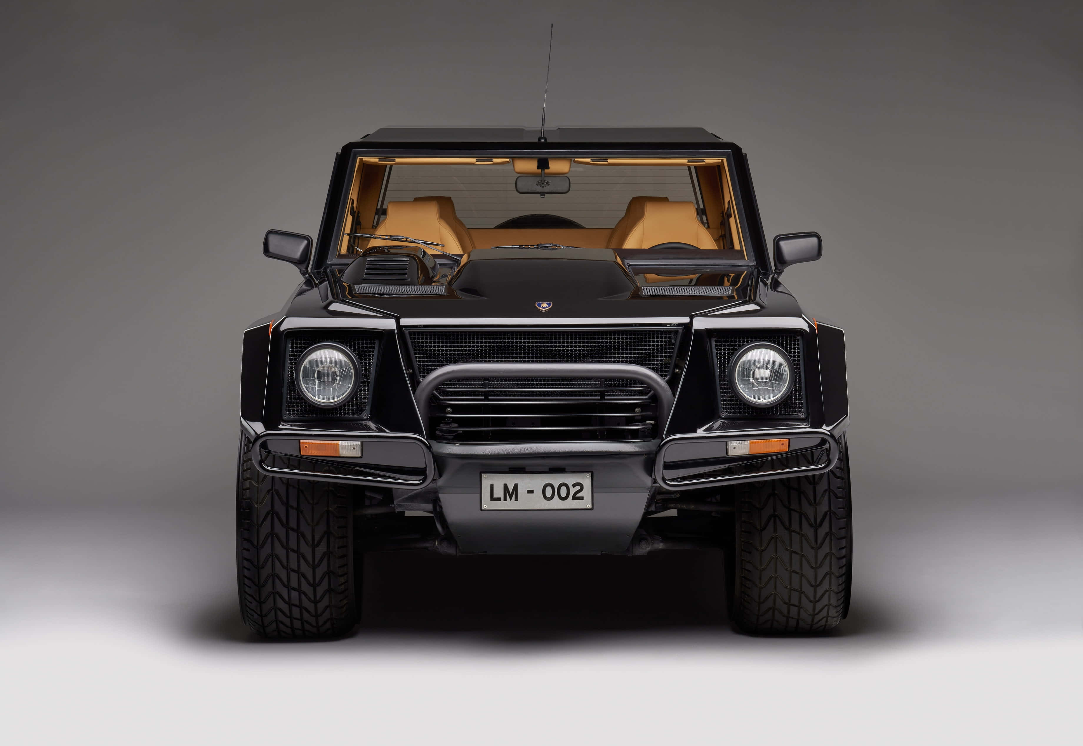 Lamborghini Lm002 桌布 壁紙 — 黑色林寶堅尼LM002的正面視圖，配以棕褐色皮革座椅和鍍鉻裝飾，背景為中性灰色工作室背景。