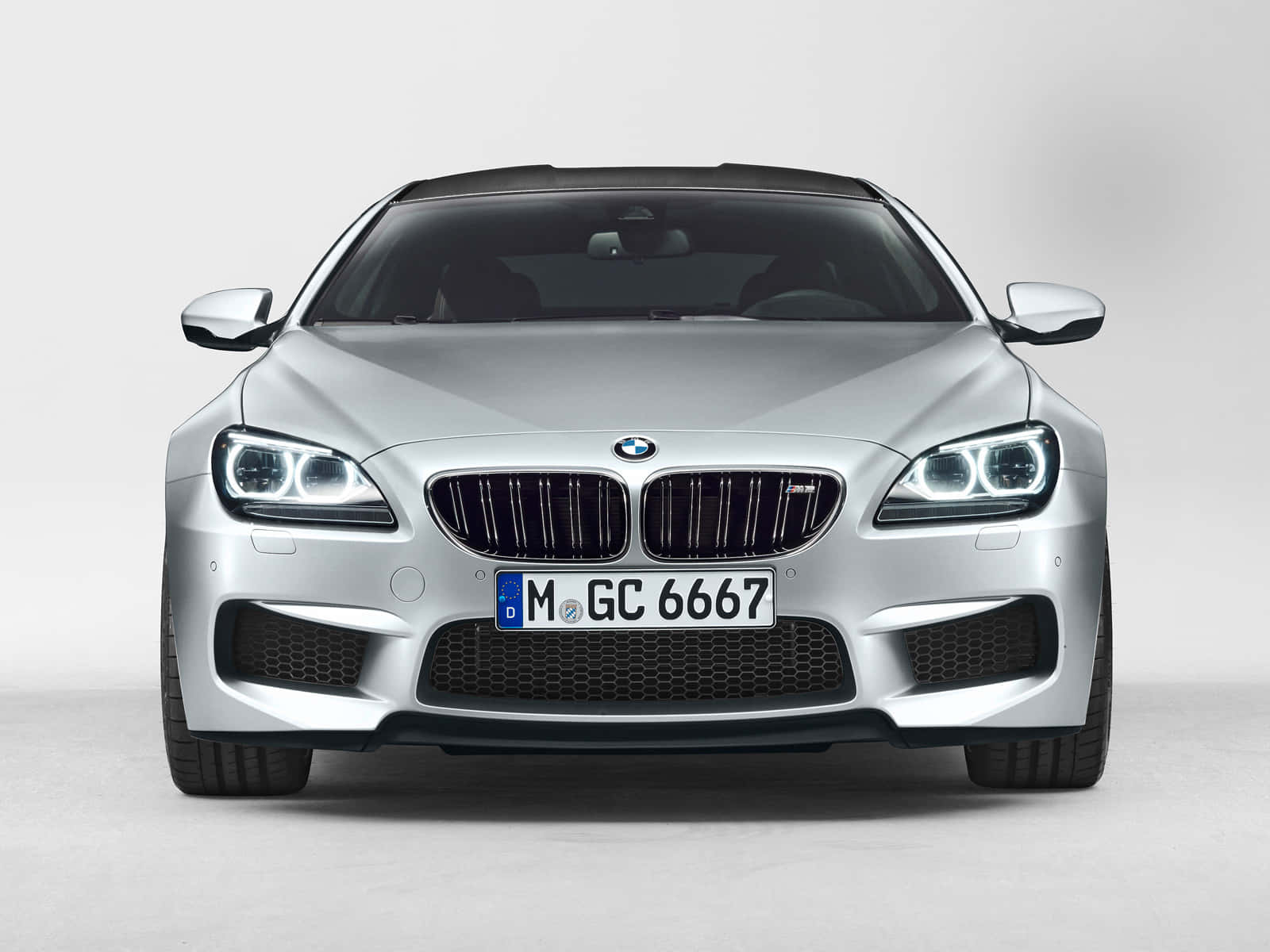 Bmw M6 桌布 壁紙 — 時尚銀色寶馬6系轎跑車的前視圖，帶有發光頭燈，背景為簡約白色工作室。
