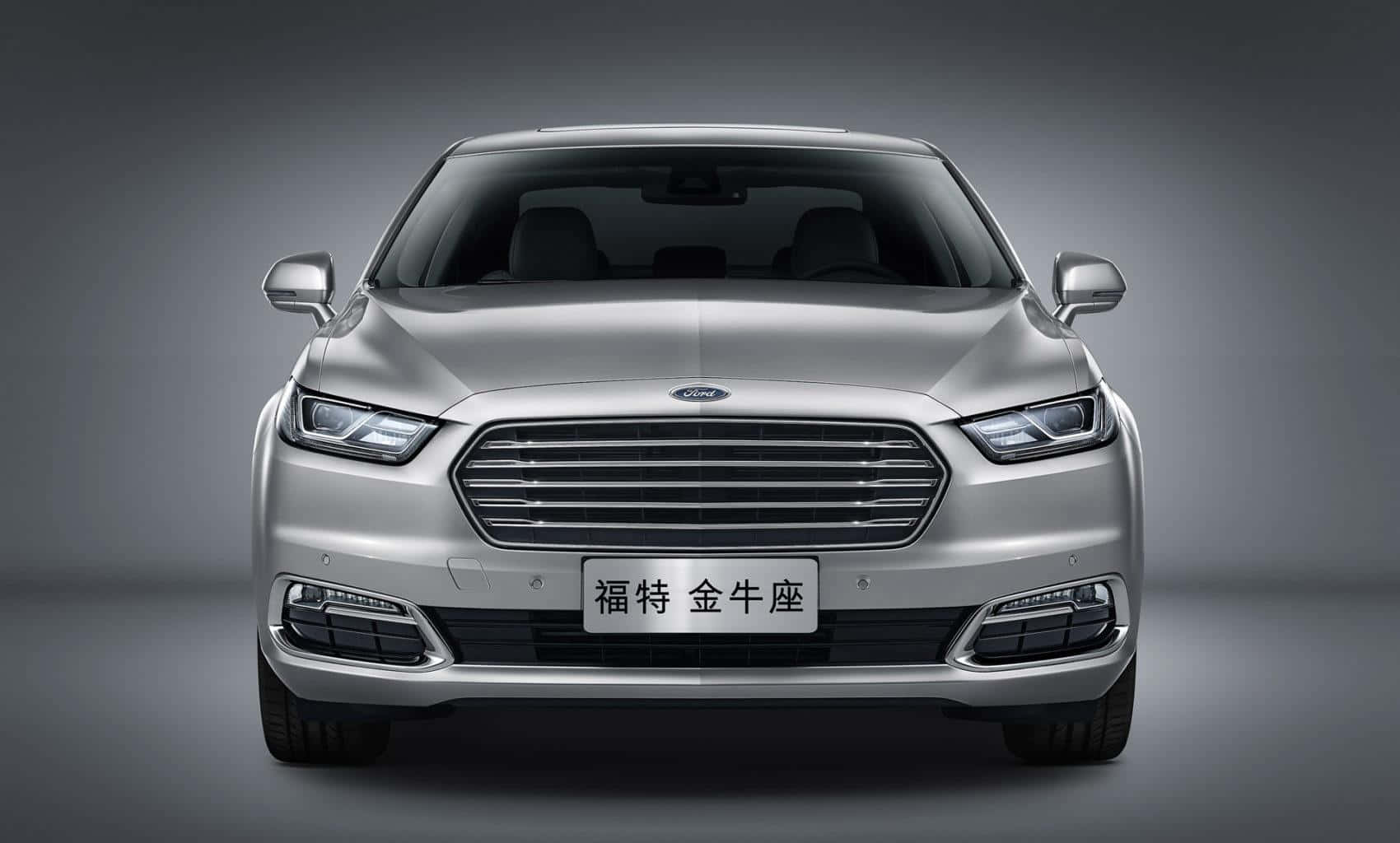 Ford Taurus 桌布 壁紙 — 銀色福特 Taurus 轎車正面視圖，配備現代化頭燈和鬼面罩，背景為漸變灰色工作室背景。