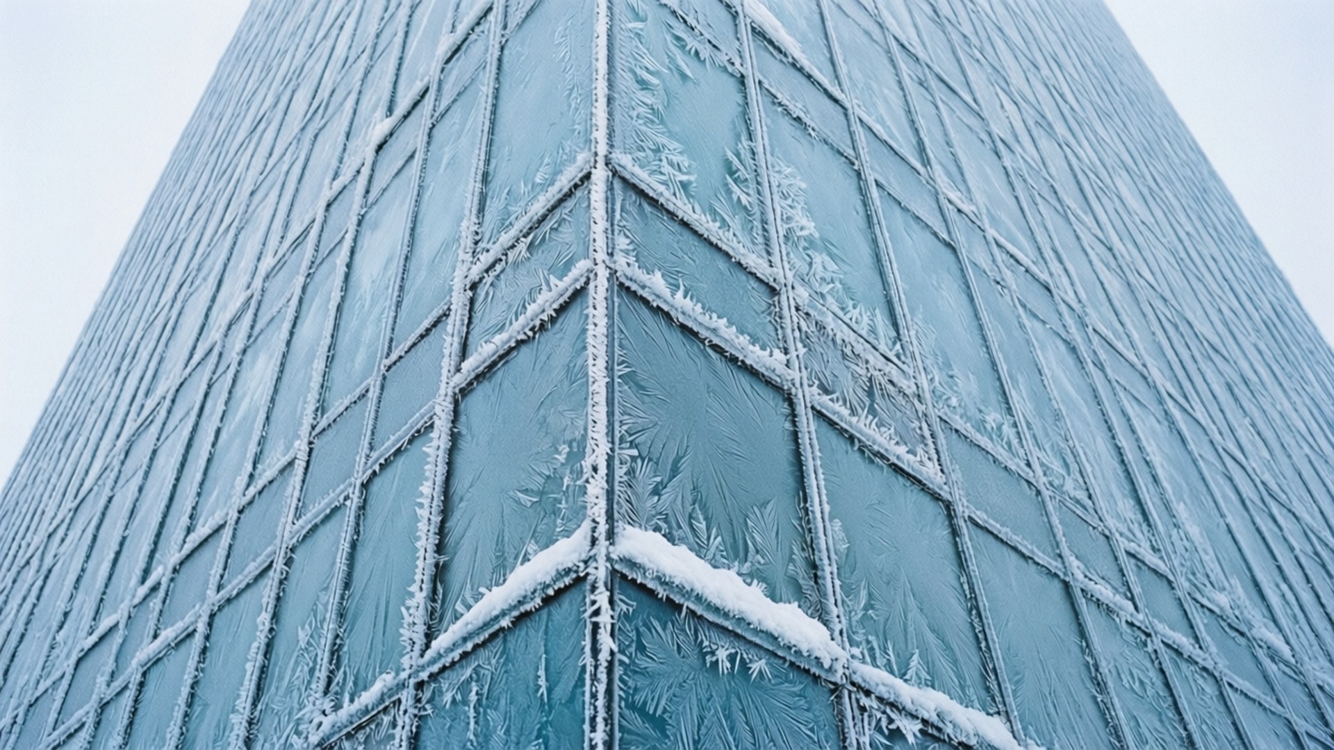 灰色天空下，一個高層玻璃建築角落覆蓋著霜和雪。