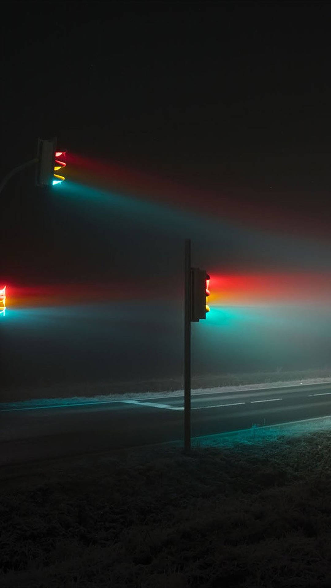 交通燈在寒冷的夜晚道路上透過薄霧發出紅色和青綠色的光芒。