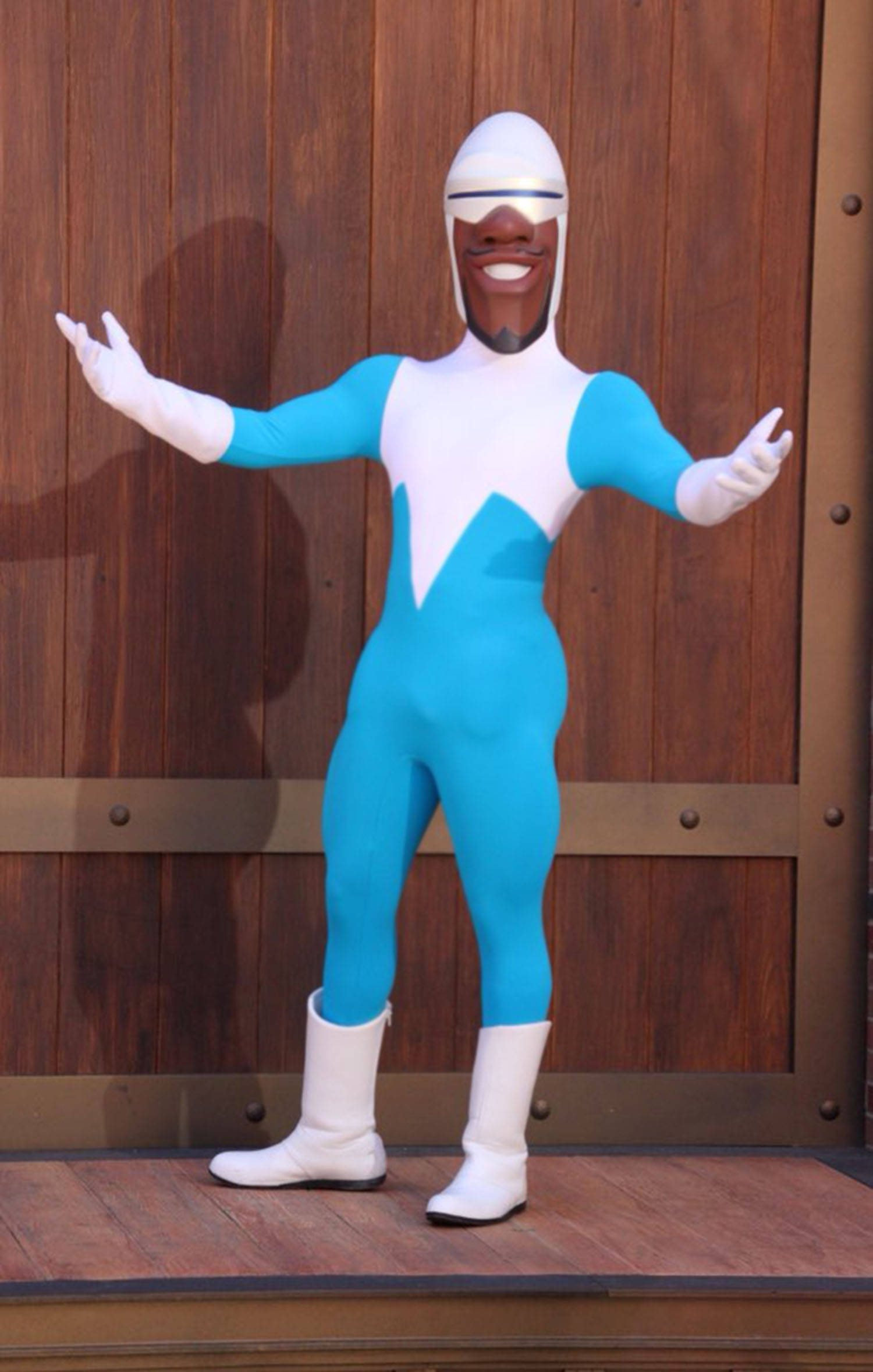 Frozone 展現超能力 壁紙 — 一個穿著藍白色超級英雄服裝嘅開心人物，企喺木門背景前，雙臂伸展。