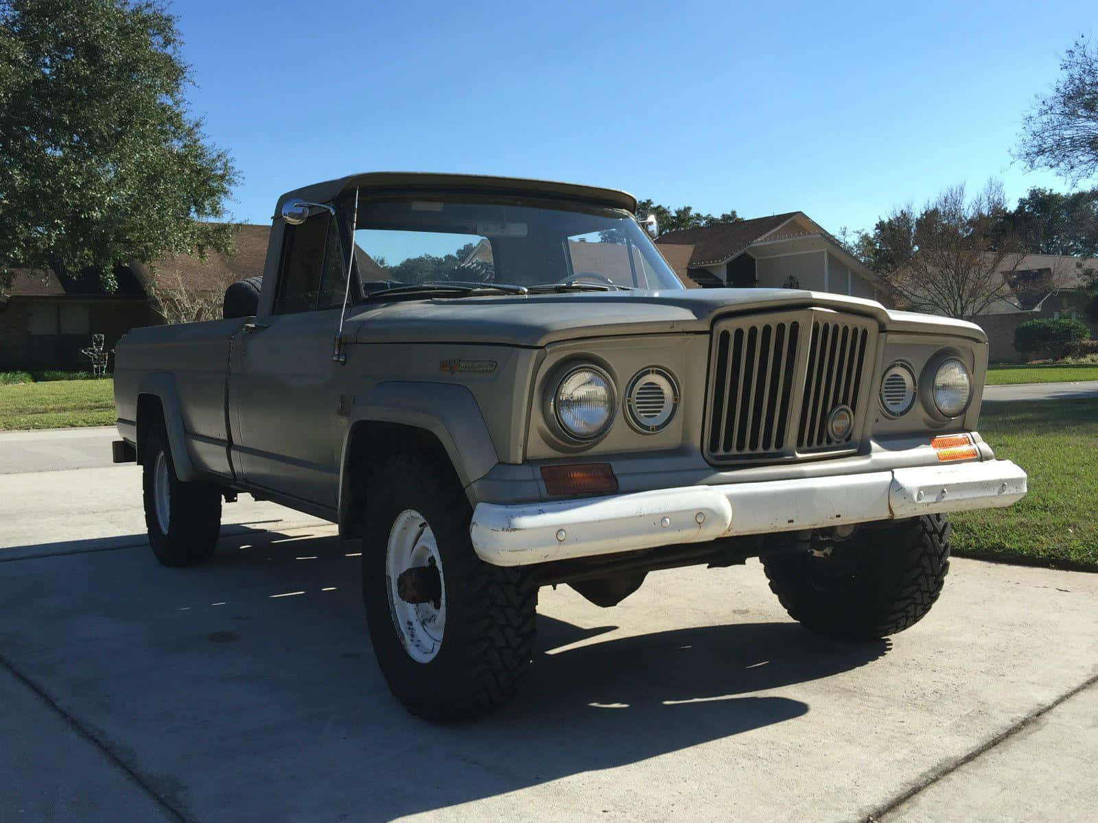 Jeep Gladiator 桌布 壁紙 — 一輛復古橄欖綠色的Jeep皮卡車，帶有白色保險槓和大輪胎，停在陽光明媚的混凝土車道上。