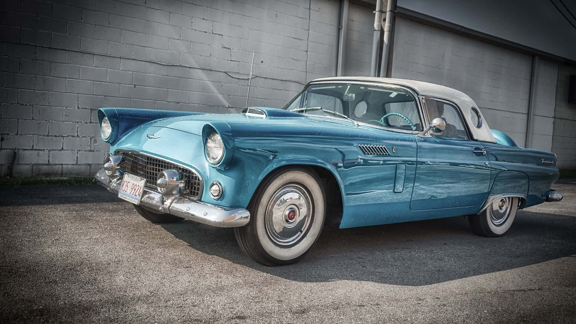 Ford Thunderbird 桌布 壁紙 — 一輛復古藍綠色福特雷鳥敞篷車停在灰色磚牆前，鍍鉻裝飾在日光下閃閃發光。