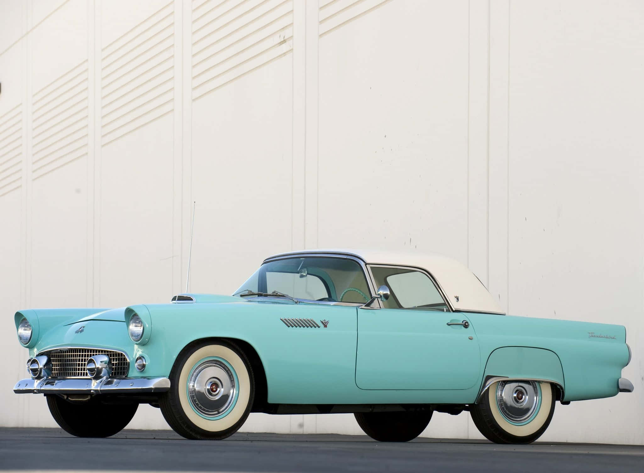Ford Thunderbird 桌布 壁紙 — 一輛復古青綠色敞篷車，白色車頂和白色輪胎，停放在白色板條牆前。