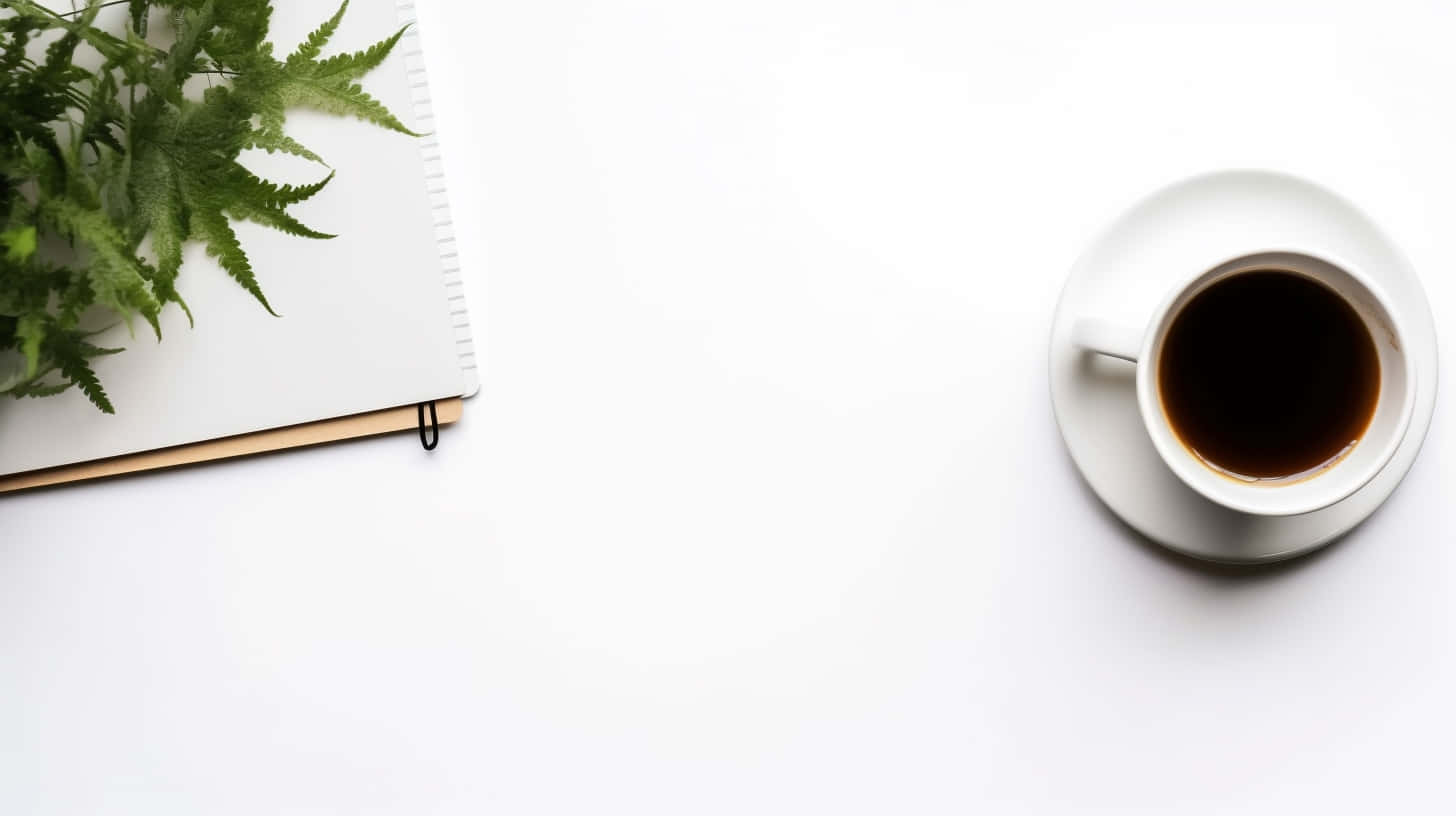 Minimalist Tea 桌布 壁紙 — 俯視角度下，白色咖啡杯旁邊放著筆記本和綠色蕨類植物，置於簡約白色表面上。