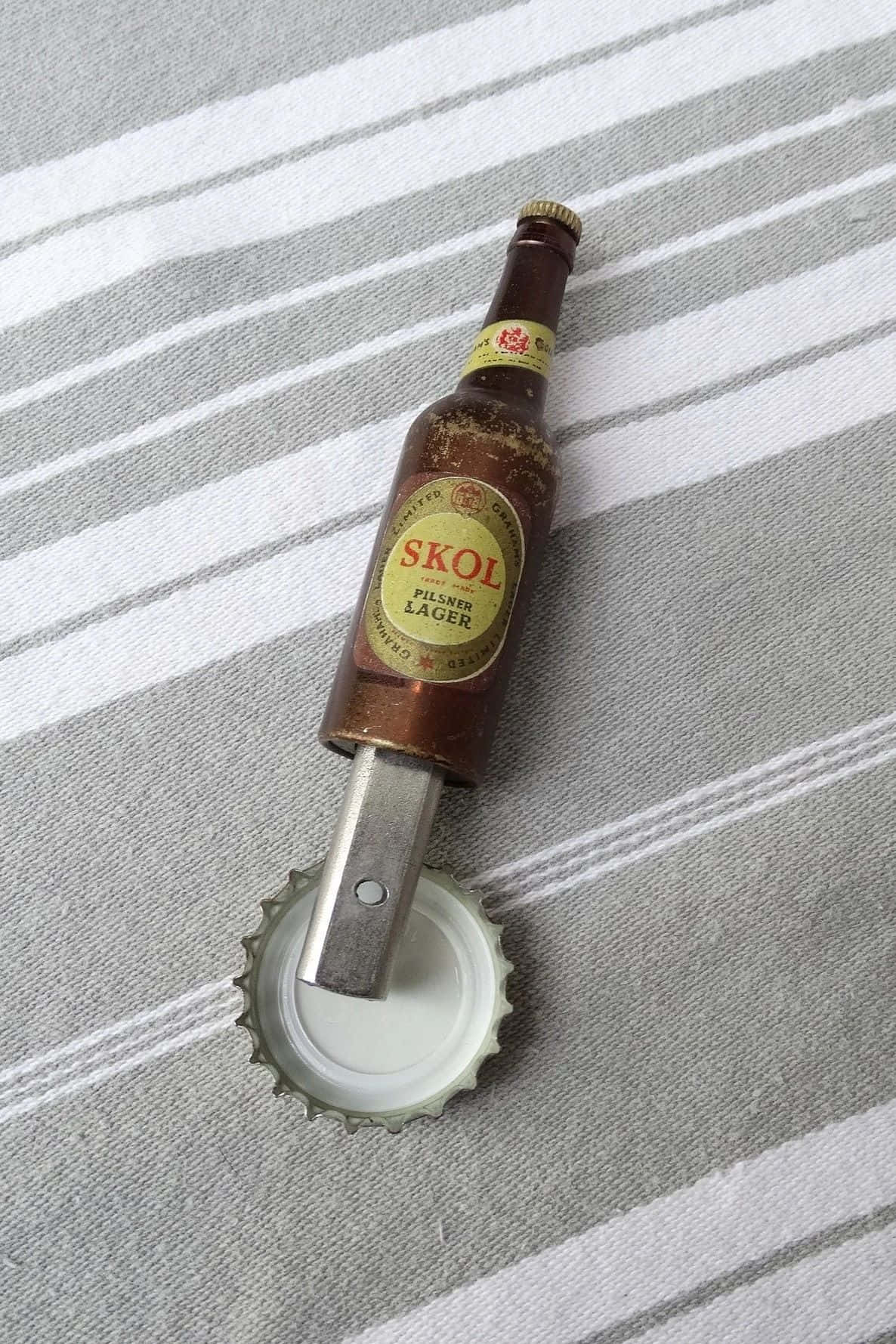  壁紙 — 一個復古SKOL啤酒瓶形開瓶器放在條紋布上，旁邊有一個分離的瓶蓋。