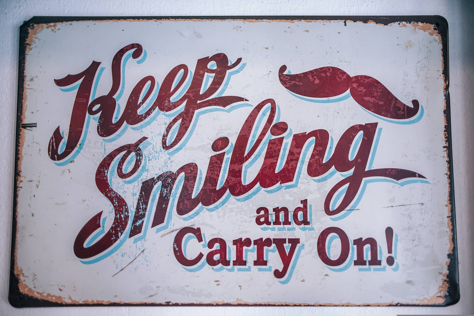生鏽復古標誌，紅色草書文字和鬍子，寫著 Keep Smiling and Carry On
