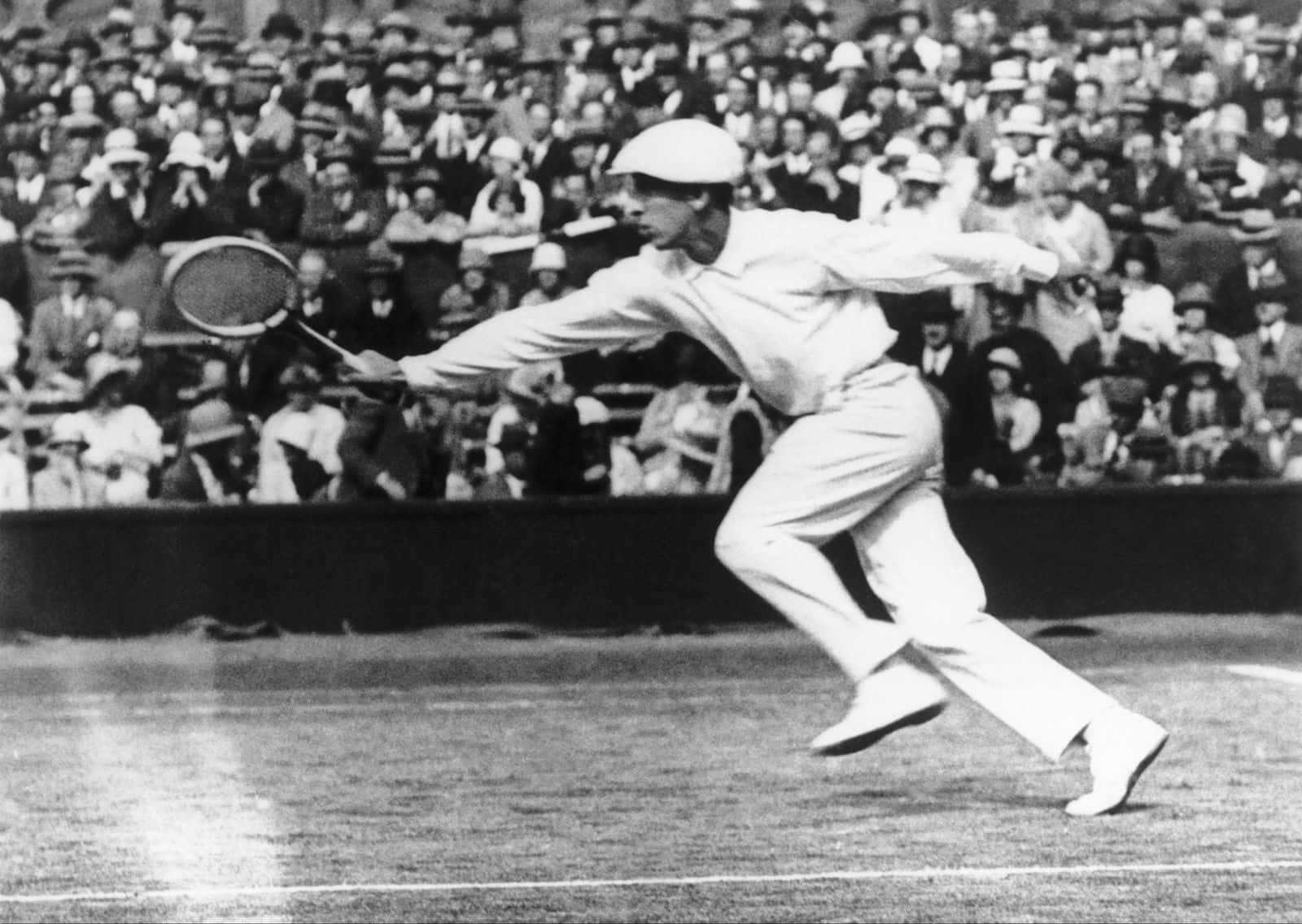 René Lacoste 持拍奔跑擊球 壁紙 — 一張復古黑白照片，顯示一名男網球手在擠滿人群的比賽中向前撲出正手擊球。