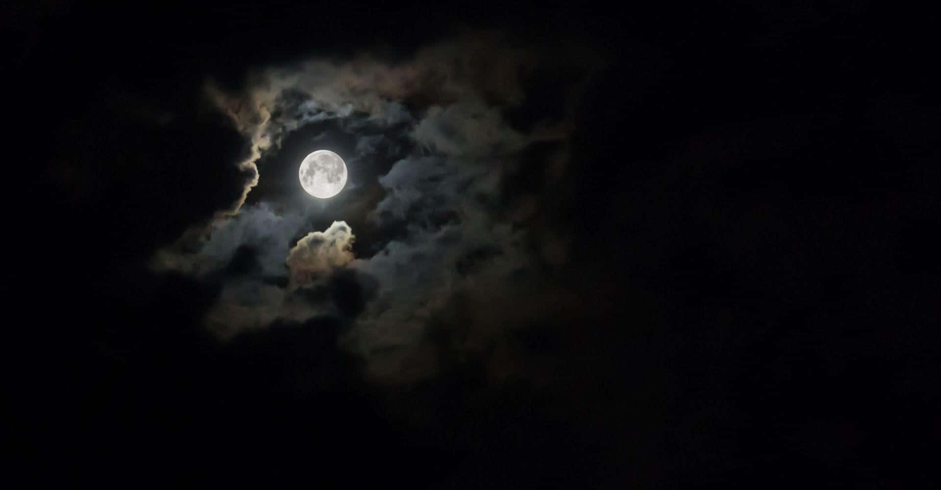 滿月在漆黑的夜空中飄動的雲層後發光。