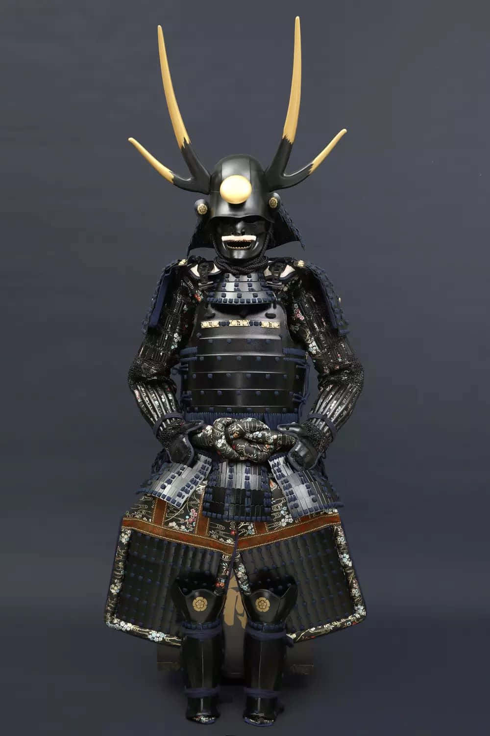  壁紙 — 一套完整的武士盔甲，配有黑色漆面甲片和金色角盔，立於深灰色工作室背景前。
